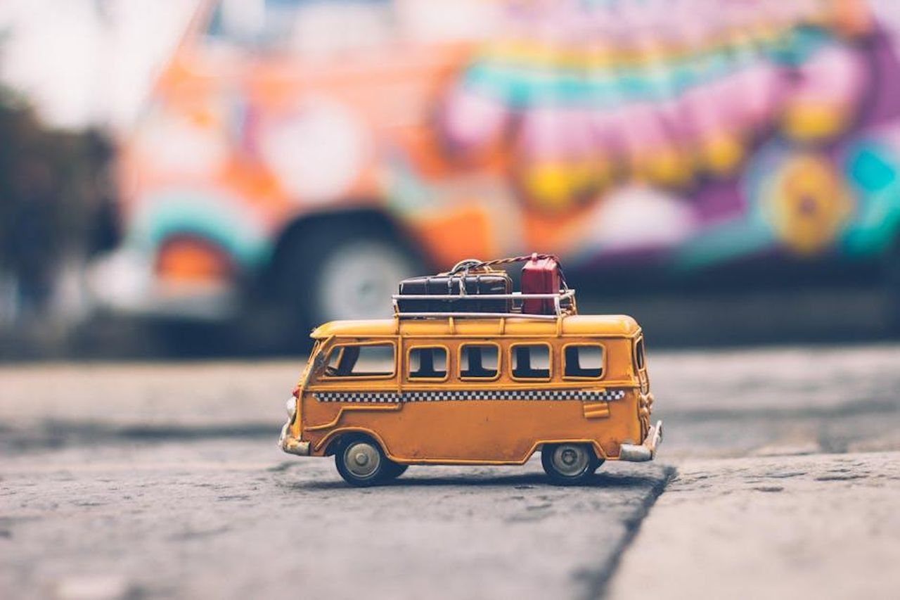 Prezzi_e_varianti_del_Volkswagen_IDBuzz_EckJVQR5lK - Veicoli24 Source: Nubia Navarro (nubikini) - pexels - Close-up of a toy Volkswagen van with luggage, set against a colorful street backdrop, evoking summer travel vibes.