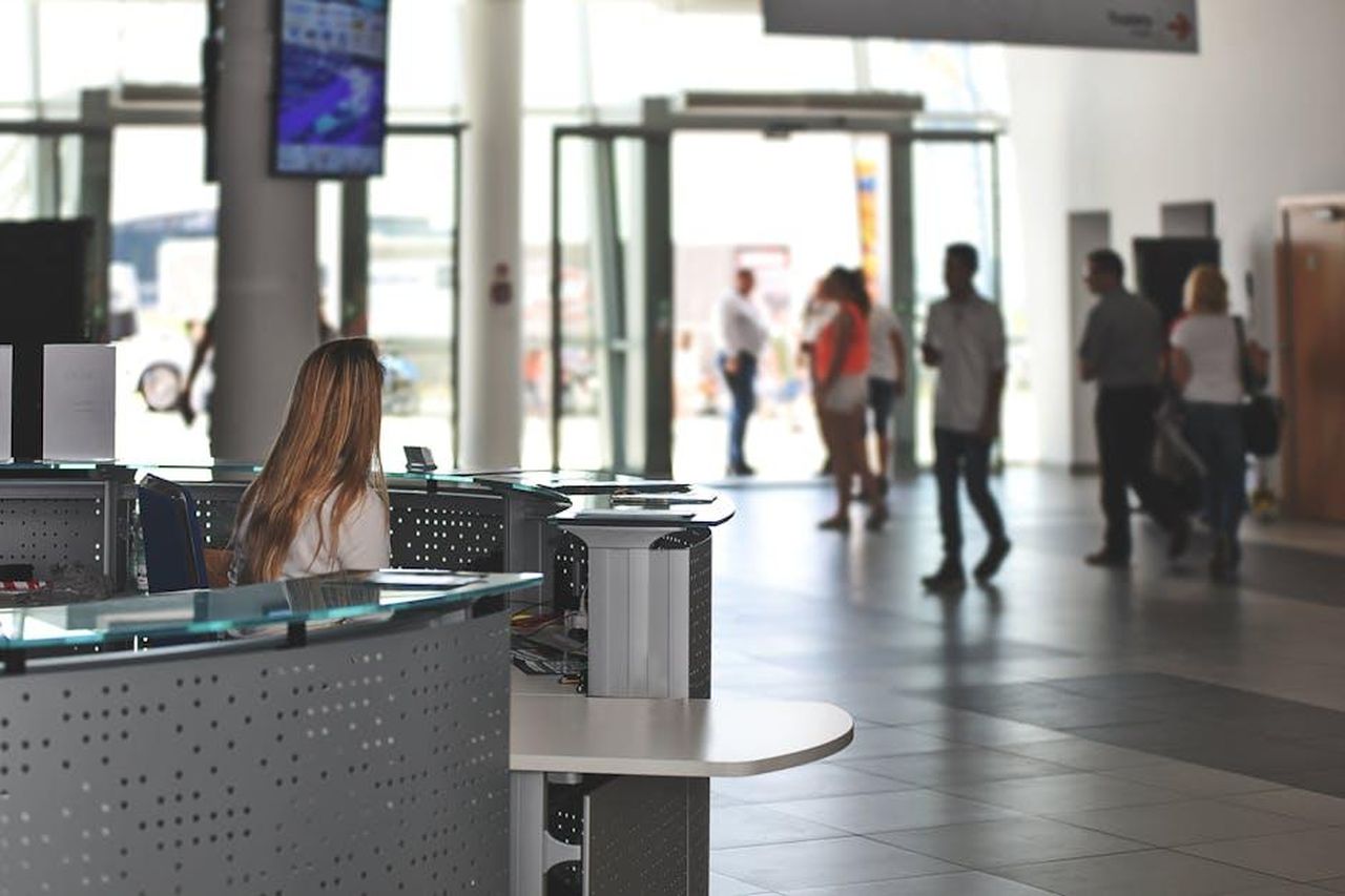 Procedura_di_richiamo_e_assistenza_clienti_9FwzTPfa9A - Veicoli24 Source: AS Photography - pexels - A bustling office reception area with people walking and a receptionist at a modern desk.