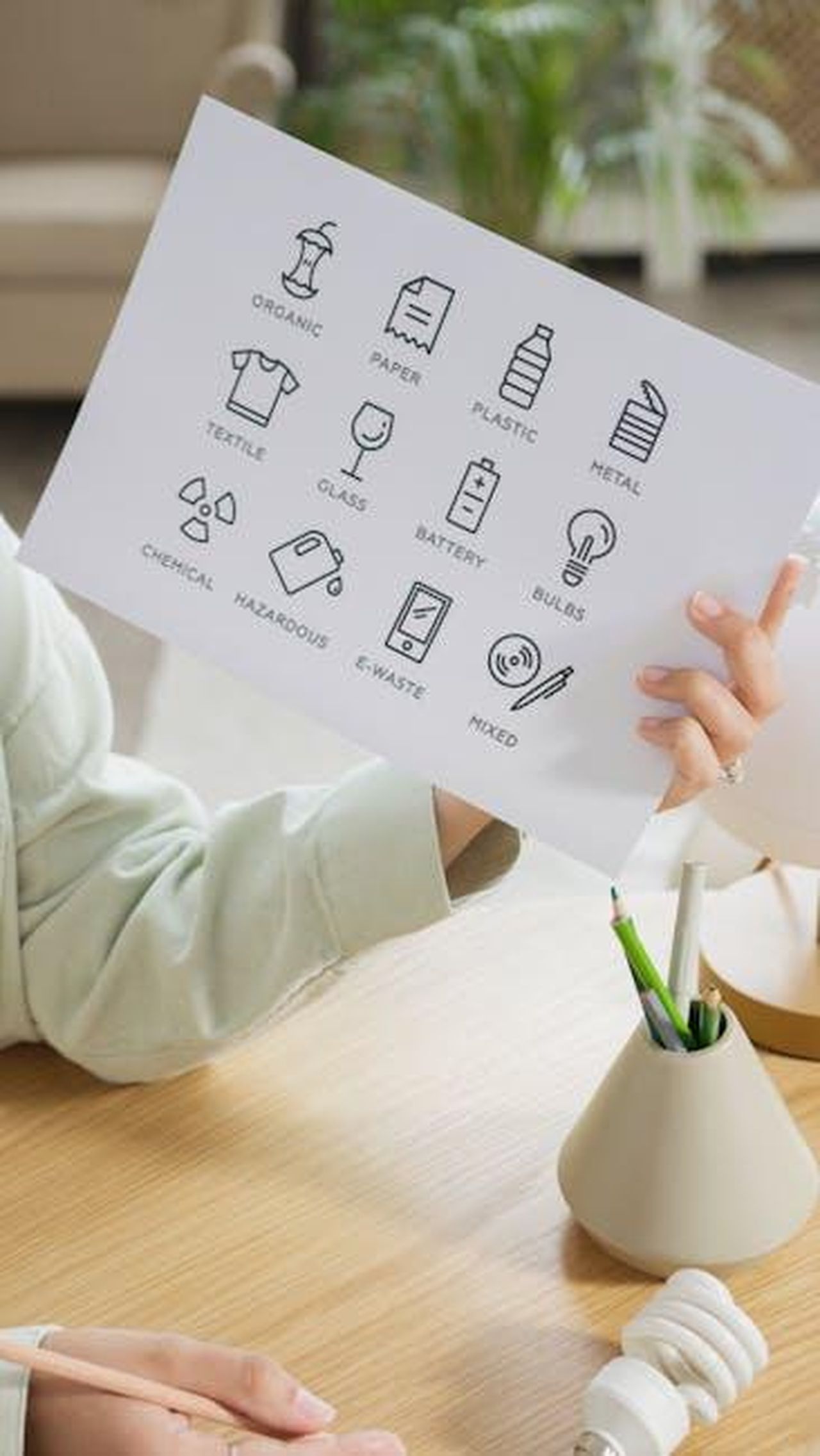 Processi_di_riciclo_innovativi_nella_catena_del_valore_ARPjkNXhhp - Veicoli24 Source: Artem Podrez - pexels - Close-up of a person holding a paper with recycling symbols above a wooden table.