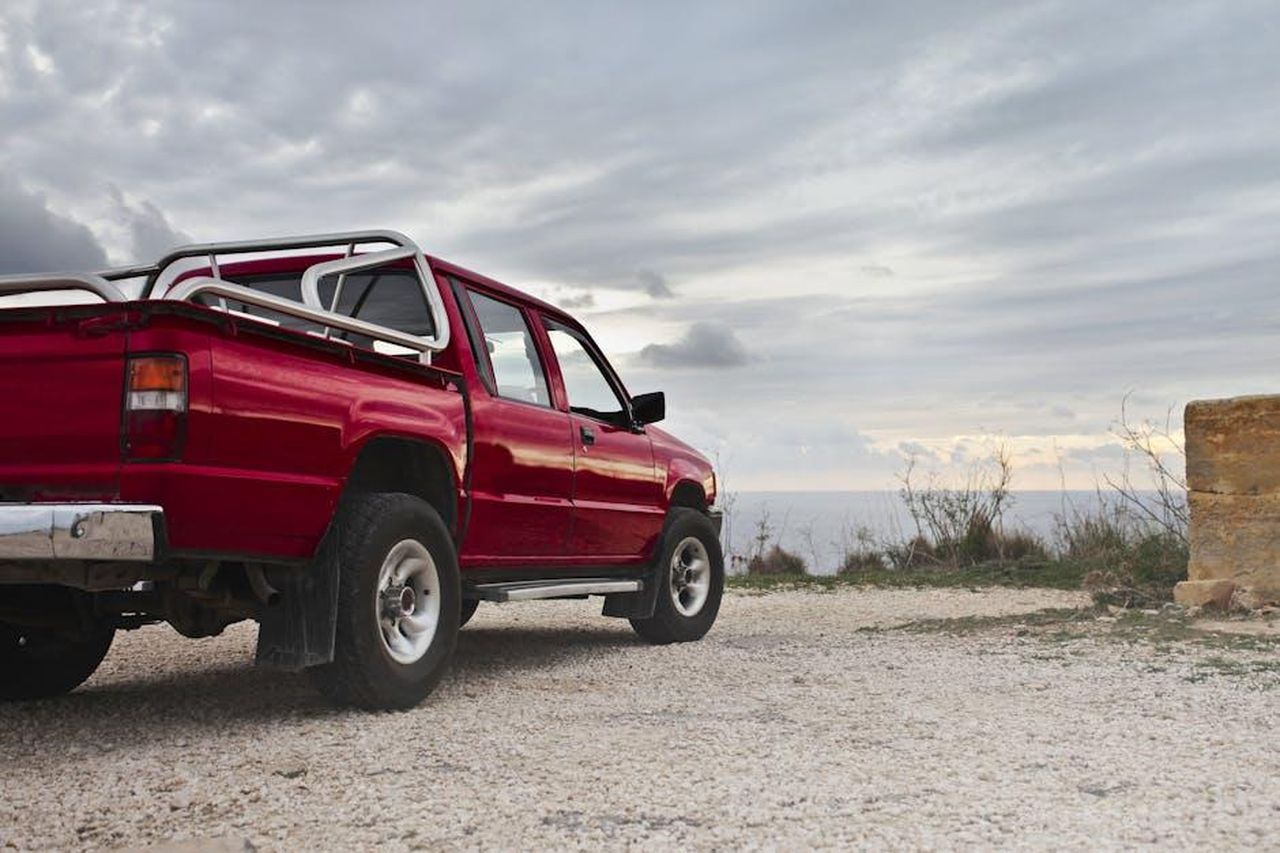 Produzione_e_mercati_del_Ford_Ranger_Super_Duty_kUNGVEGGbZ - Veicoli24 Source: Andrea Piacquadio - pexels - A red pickup truck parked by the rocky coastline under a cloudy sky in Mgarr, Malta.