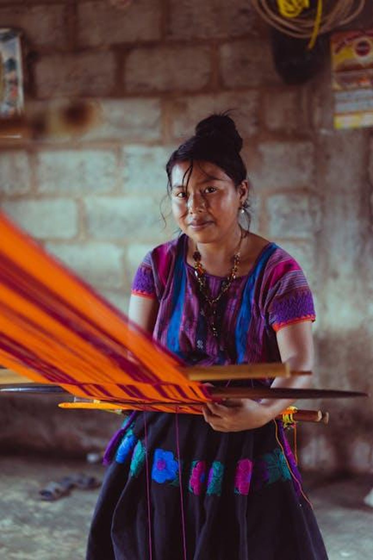 Produzione_in_Messico_e_tariffe_PXtWFqlqRB - Veicoli24 Source: Los Muertos Crew - pexels - Indigenous Mexican woman weaving colorful fabric on a traditional loom inside a rustic setting.