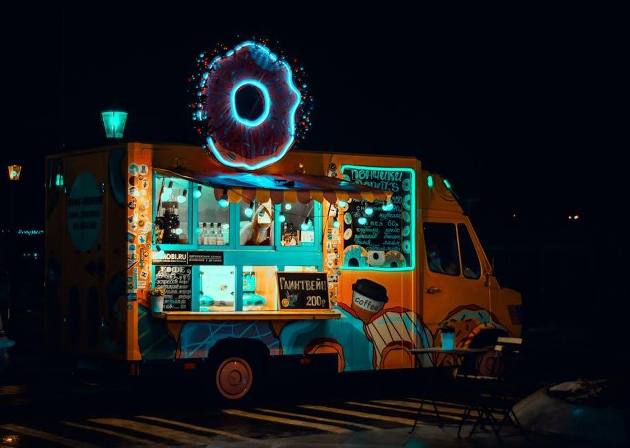Prospettive_per_il_mercato_dei_veicoli_elettrici_UfdfHw5ekY - Veicoli24 Source: Artem Saranin - pexels - Vibrant neon food truck at night serving snacks with glowing donut sign.