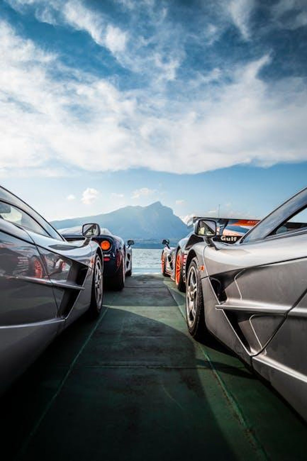 Punti_di_forza_EAMdGcUzLd - Veicoli24 Source: Quentin Martinez - pexels - Stunning lineup of supercars on a lakeside road with mountain views, perfect for automobile enthusiasts.