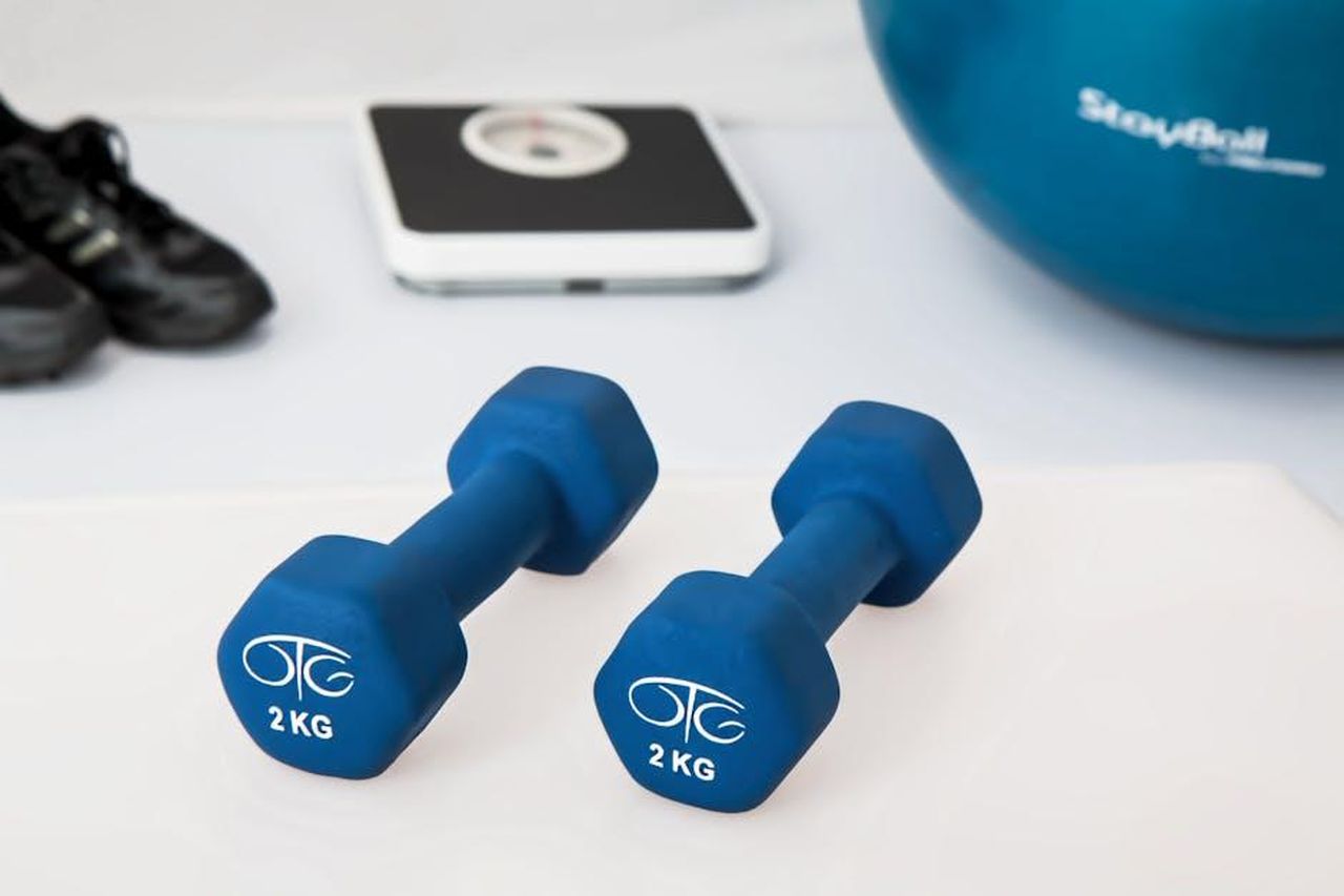Punti_di_forza_della_Polestar_2_fYfhRNXXQj - Veicoli24 Source: Pixabay - pexels - Blue dumbbells placed on a white surface with fitness equipment in the background.