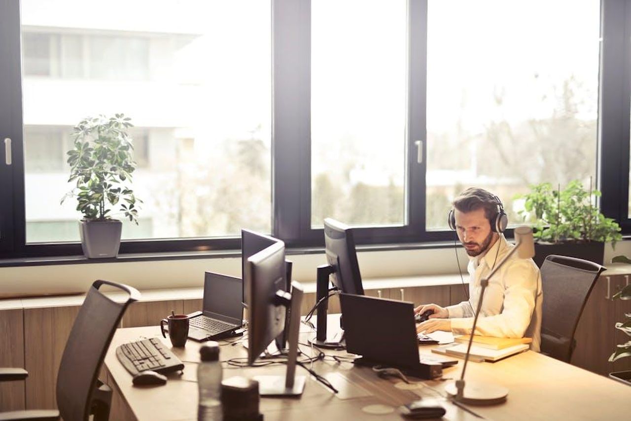 Puoi_dimostrare_come_hai_supportato_i_tuoi_clienti_vulnerabili_8SYaTkshvi - Veicoli24 Source: Andrea Piacquadio - pexels - A businessman sits at a desk using multiple computers and a headset in a well-lit modern office.
