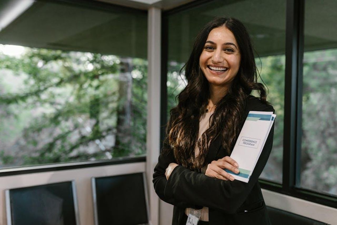 Registrazione_e_opportunit_per_sviluppatori_f6G4YkssoO - Veicoli24 Source: RDNE Stock project - pexels - Confident woman holding conference program, smiling in modern indoor setting.