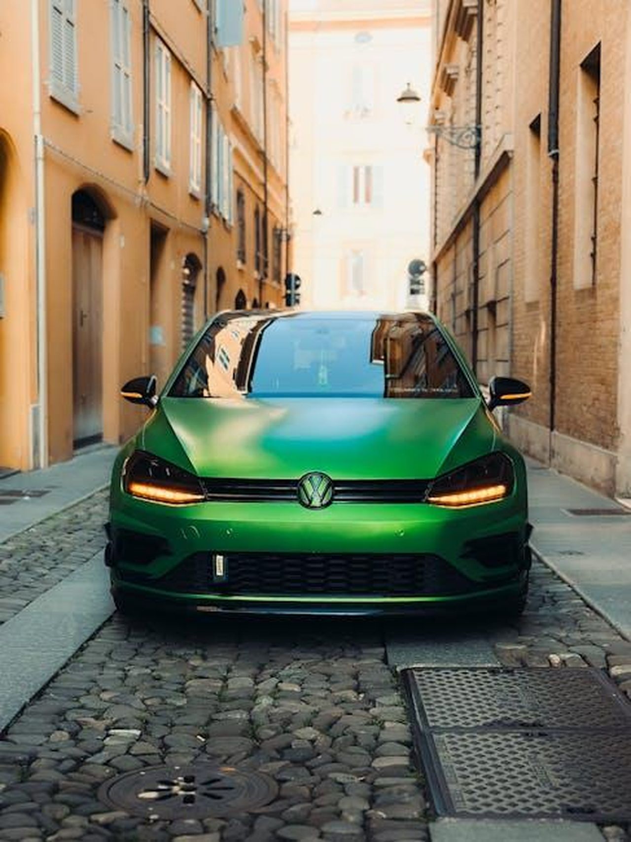 Retrofit_gratuito_per_i_proprietari_esistenti_NxPEPsLIYi - Veicoli24 Source: Borta - pexels - A vibrant green car parked in a narrow European alley with cobblestone pavement.