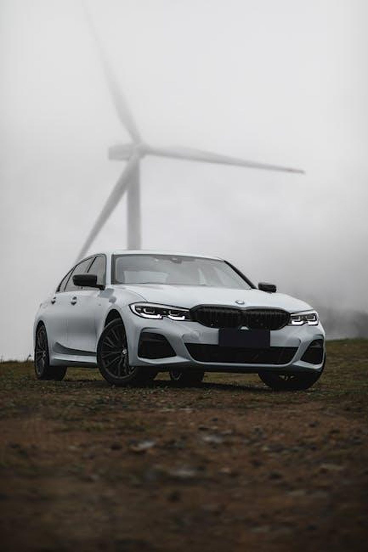 Riconoscimenti_per_il_nuovo_BMW_3_Series_HoW5pQbvNv - Veicoli24 Source: zhuzichun - pexels - A modern BMW car parked in a foggy landscape with a wind turbine in the background, capturing a blend of technology and nature.
