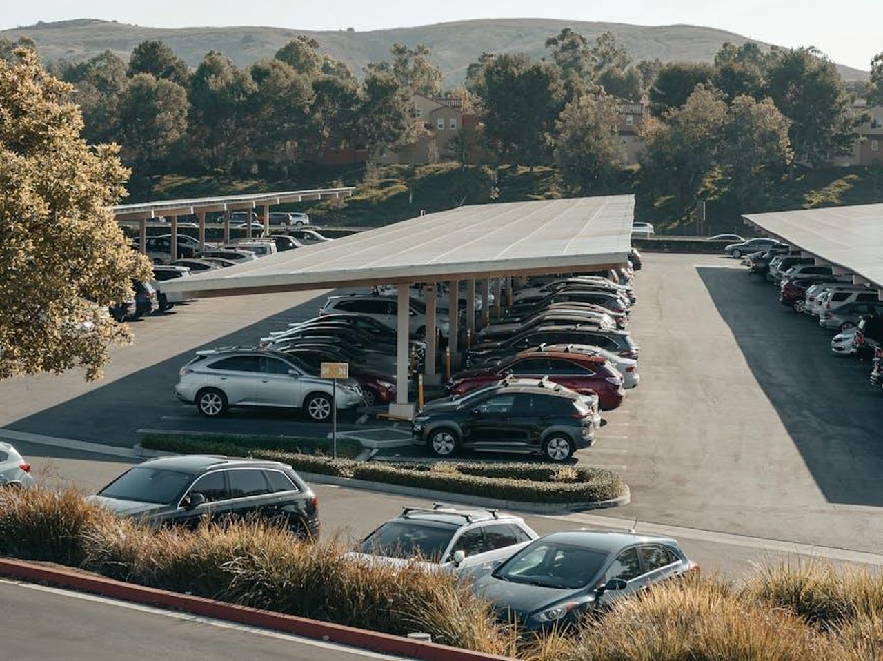 Riconsiderazione_della_produzione_di_veicoli_elettrici_da_parte_di_Nissan_6WJx3M5GlX - Veicoli24 Source: Kindel Media - pexels - View of a large parking lot with solar panel shades and diverse vehicles parked.