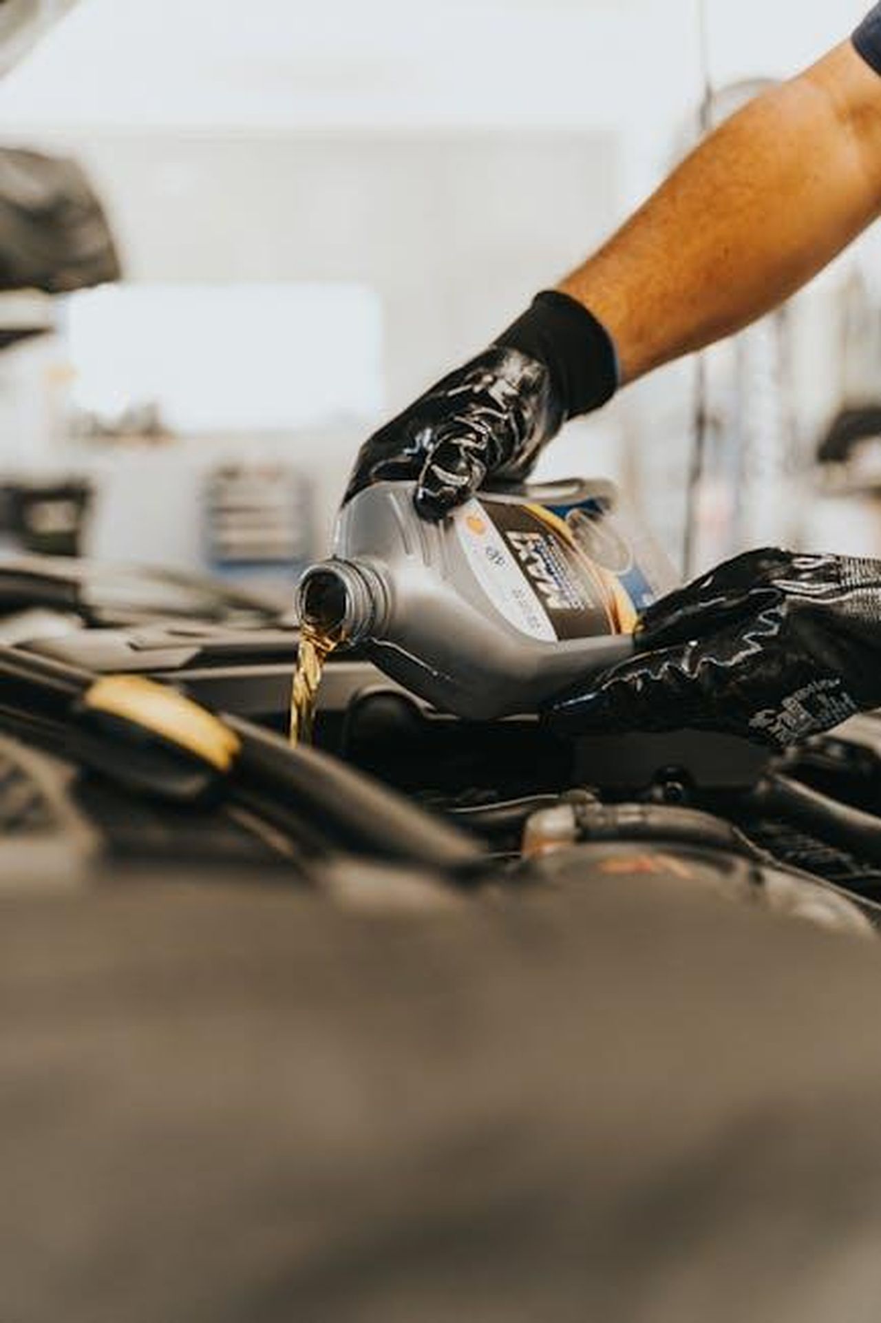 Risposta_alle_pressioni_del_mercato_e_alla_concorrenza_J2Qr9kxzQp - Veicoli24 Source: Daniel Andraski - pexels - Close-up of a mechanic pouring engine oil into a car engine with gloved hands, indoors.