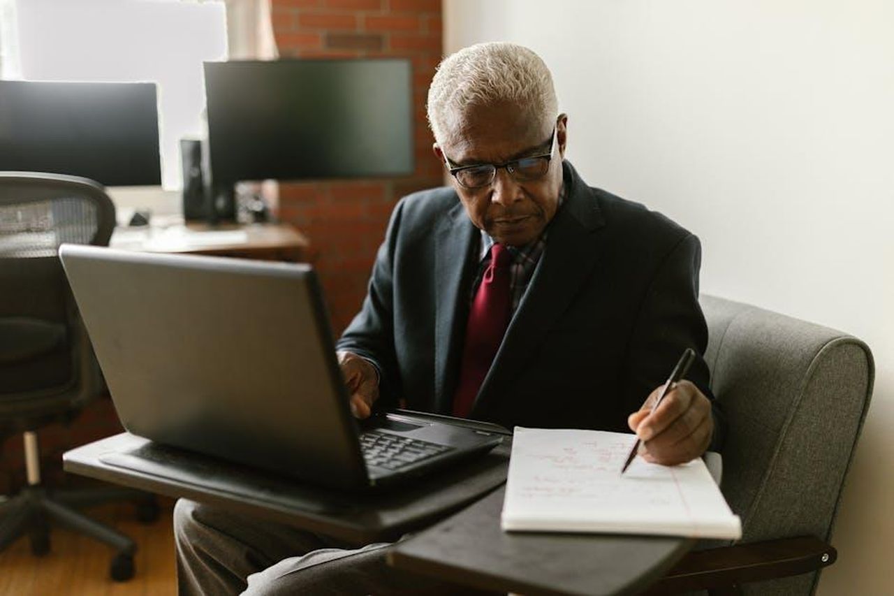 Ritiro_di_Christopher_Reynolds_e_nuovo_ruolo_x16xmdK5OW - Veicoli24 Source: RDNE Stock project - pexels - Elderly businessman in a suit writing notes while using a laptop in a modern office setting.