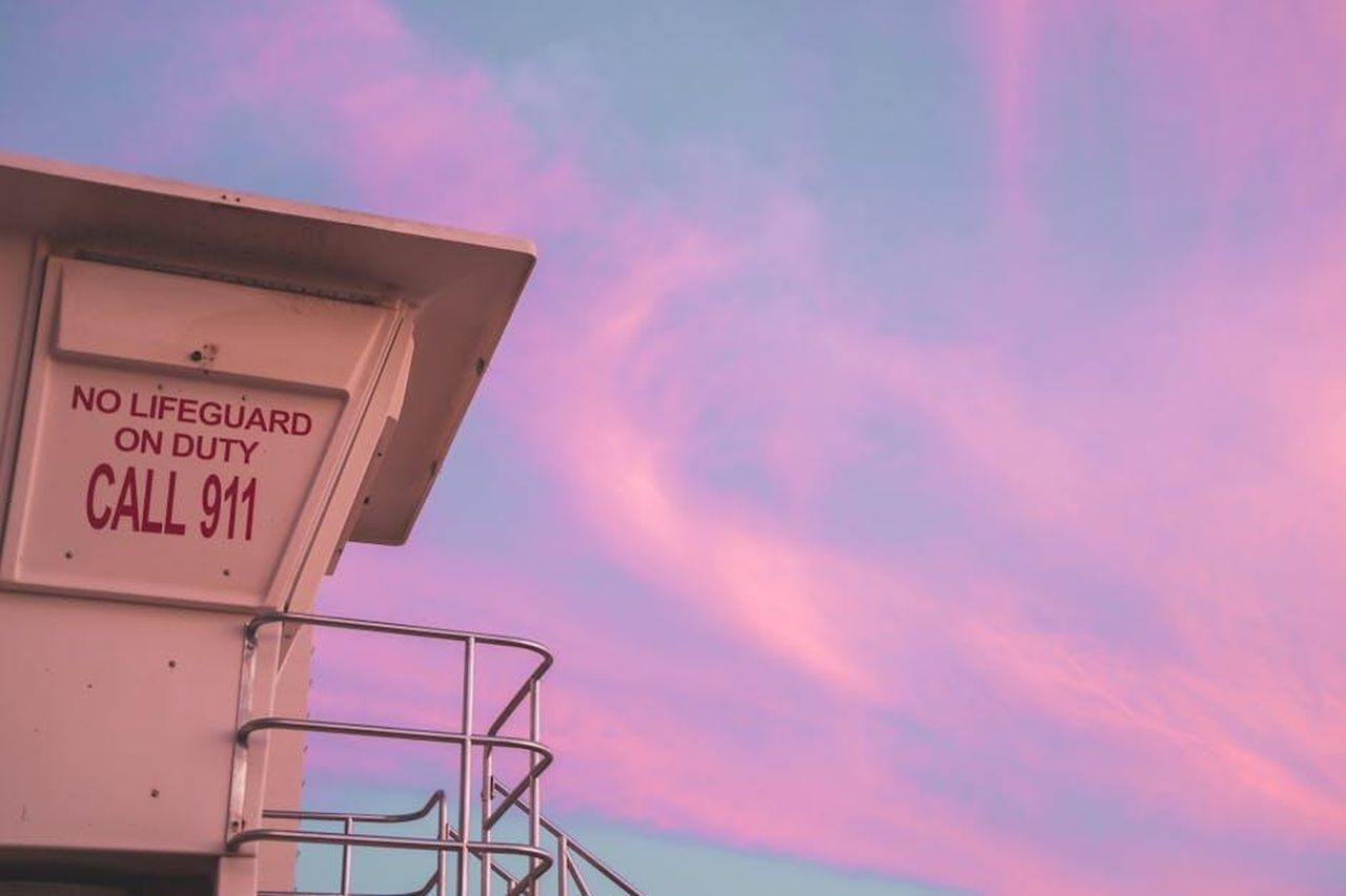 Sicurezza_mr5oRP7qmE - Veicoli24 Source: Jess Loiterton - pexels - Lifeguard tower with 'No Lifeguard on Duty' sign under a pastel pink sunset sky.