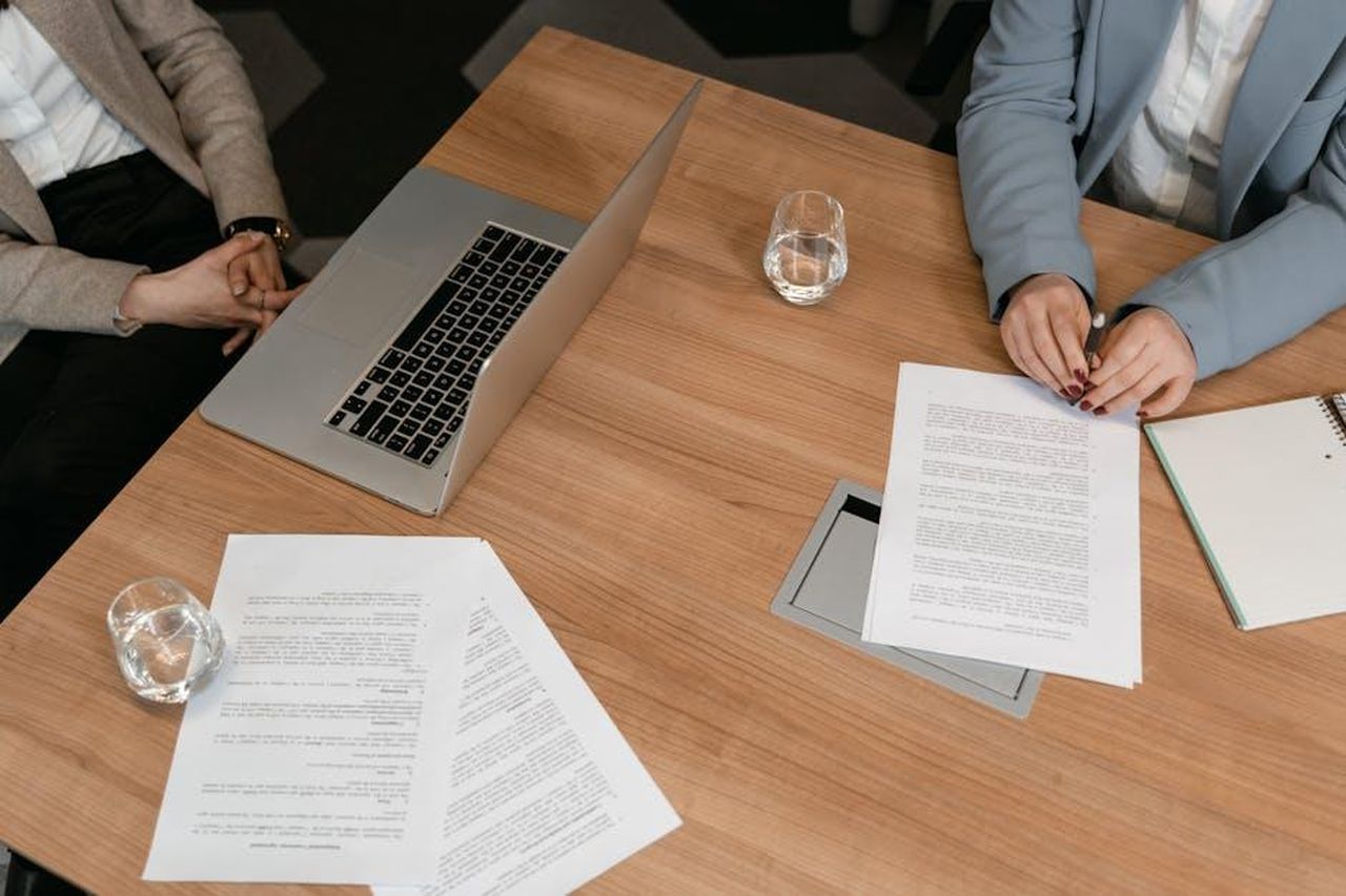 Strategia_aziendale_e_modelli_di_produzione_yvhbOuGKMh - Veicoli24 Source: MART PRODUCTION - pexels - Two professionals hold a meeting with documents and a laptop on a wooden desk.