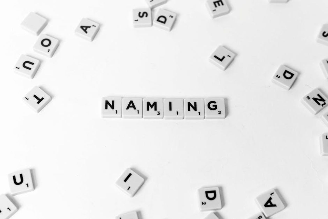 Strategia_di_denominazione_di_Alpine_lC0WlPQ6By - Veicoli24 Source: Visual Tag Mx - pexels - Flat lay of scattered Scrabble tiles spelling 'NAMING' on a white background.