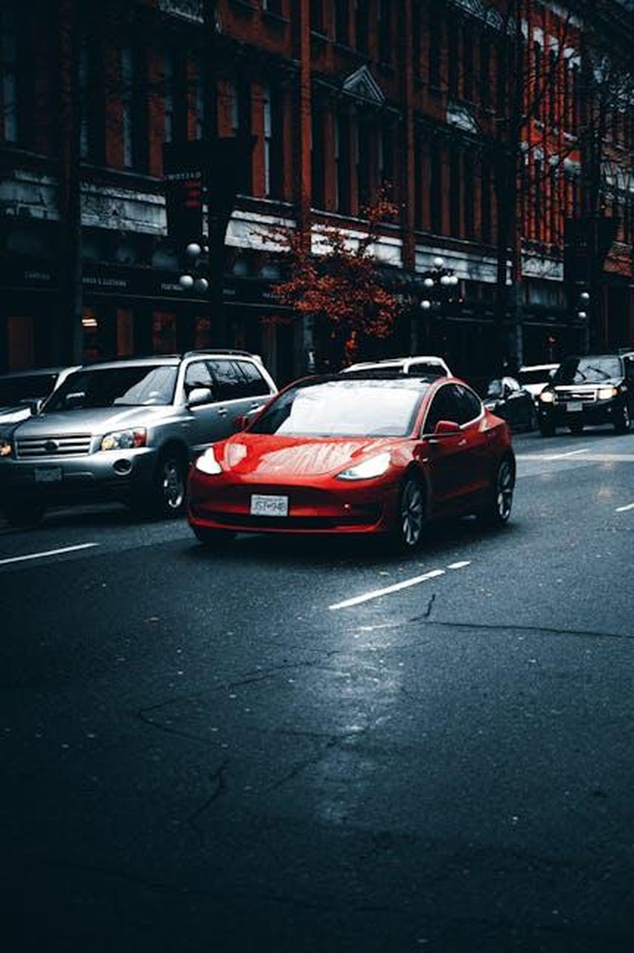 Tesla_e_la_sua_posizione_nel_mercato_hV43jgOakp - Veicoli24 Source: Luke Miller - pexels - Sleek red electric car driving on an urban street with historic buildings.