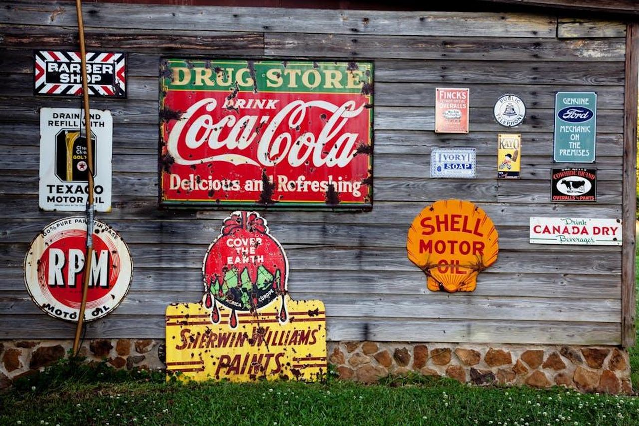 Utilizzo_della_Ford_GT_per_il_marketing_JRVb3yRKPS - Veicoli24 Source: Pixabay - pexels - Collection of vintage advertising signs on rustic wooden wall showcasing classic brands.