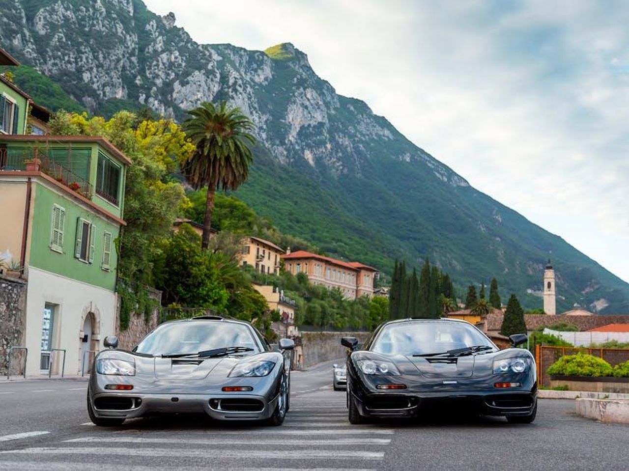 Valentino_Rossi_e_il_debutto_di_MercedesAMG_in_LMGT3_6dKlR0xHPe - Veicoli24 Source: Quentin Martinez - pexels - Two supercars in a picturesque Italian town with mountain backdrop, showcasing speed and style.