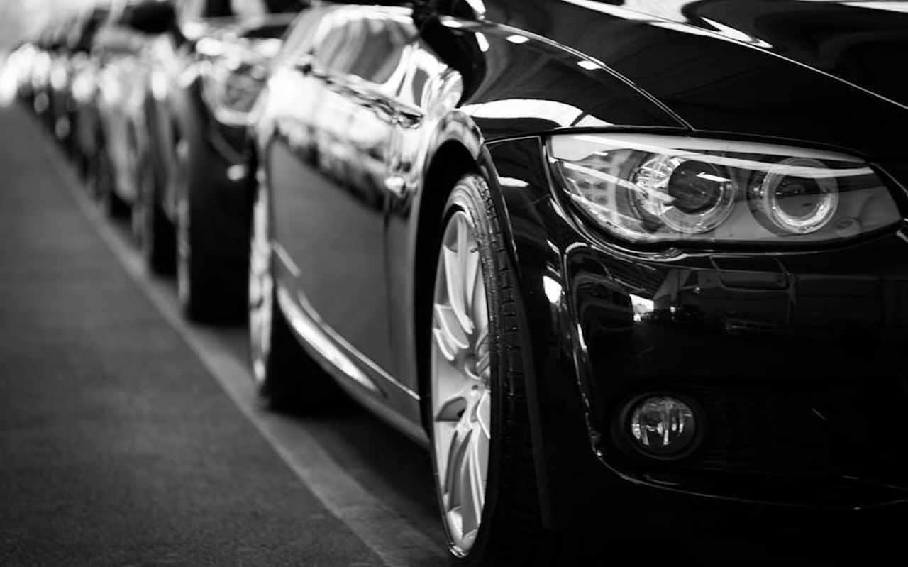 Acquisizione_del_concessionario_Stellantis_in_Arizona_uVaqBw20pY - Veicoli24 Source: Torsten Dettlaff - pexels - Close-up black and white image of a luxury car line-up focusing on vehicle headlights.