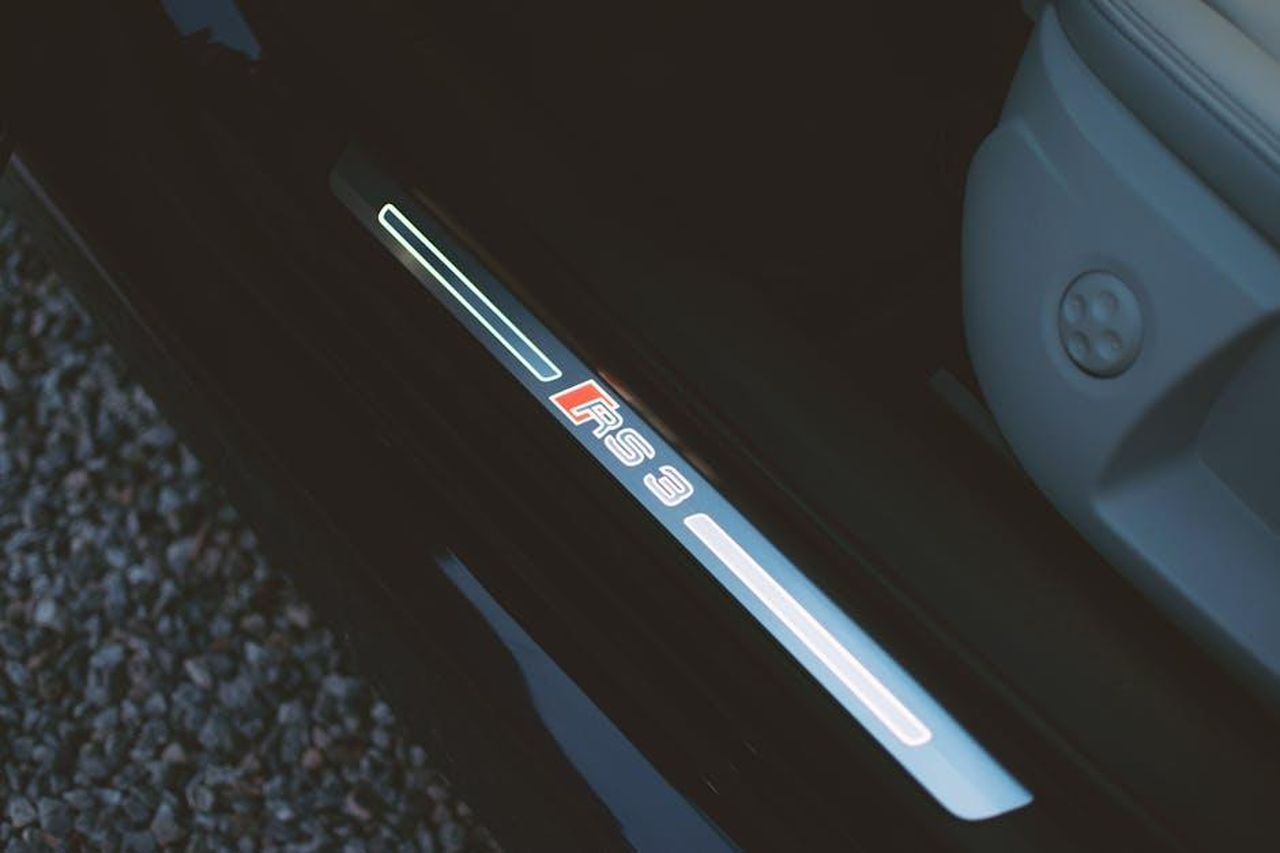 Andamento_dei_valori_di_rivendita_in_Europa_k8RQLO9a7P - Veicoli24 Source: Alexander Pöllinger - pexels - Detailed view of Audi RS3 door sill featuring illuminated logo, captured in moody lighting.