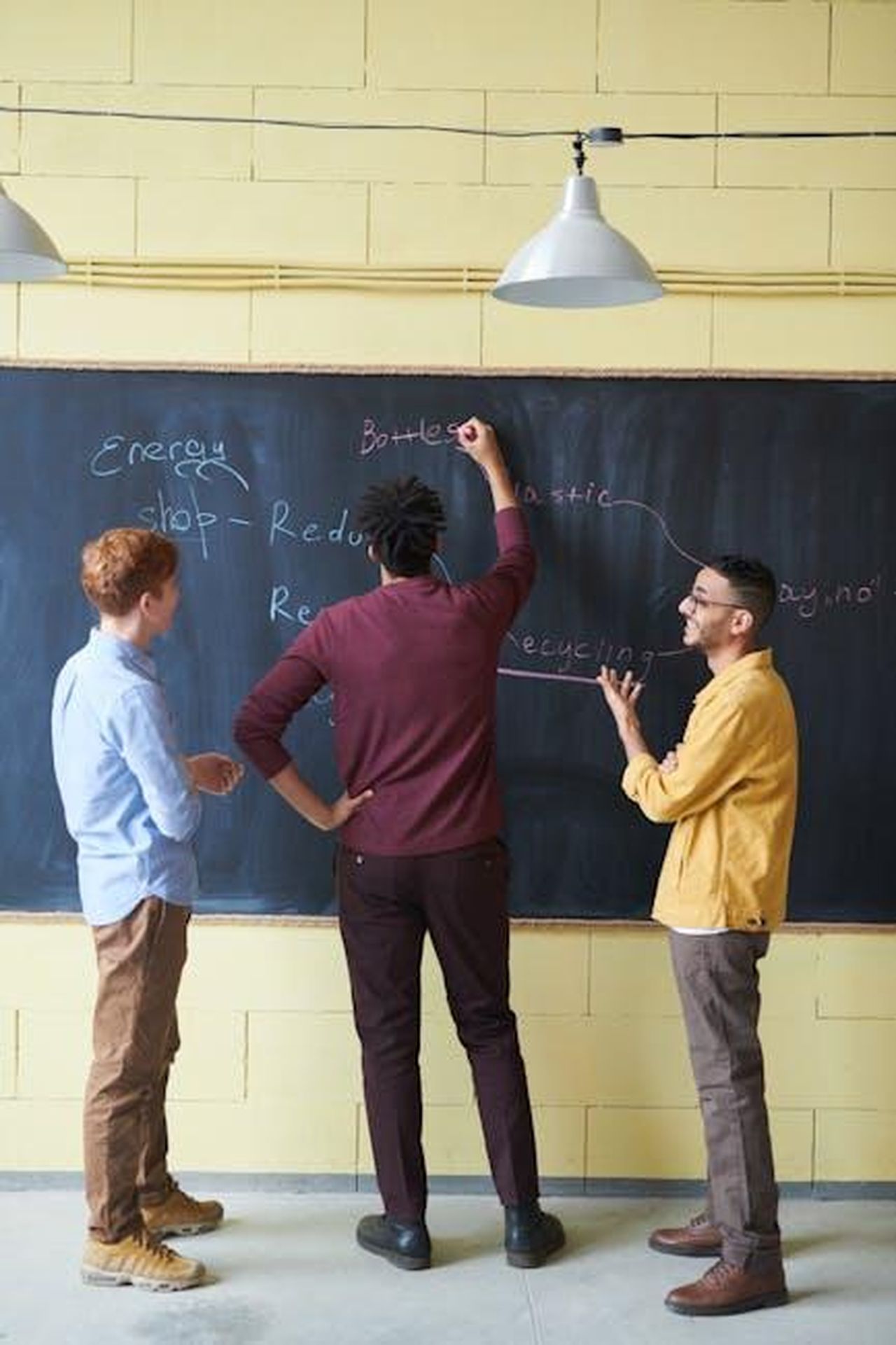 Benefici_della_Tecnologia_V2H_per_i_Clienti_Kia_EV9_nLgBUcCecO - Veicoli24 Source: fauxels - pexels - Three adults discussing strategies at a chalkboard in a modern office space.
