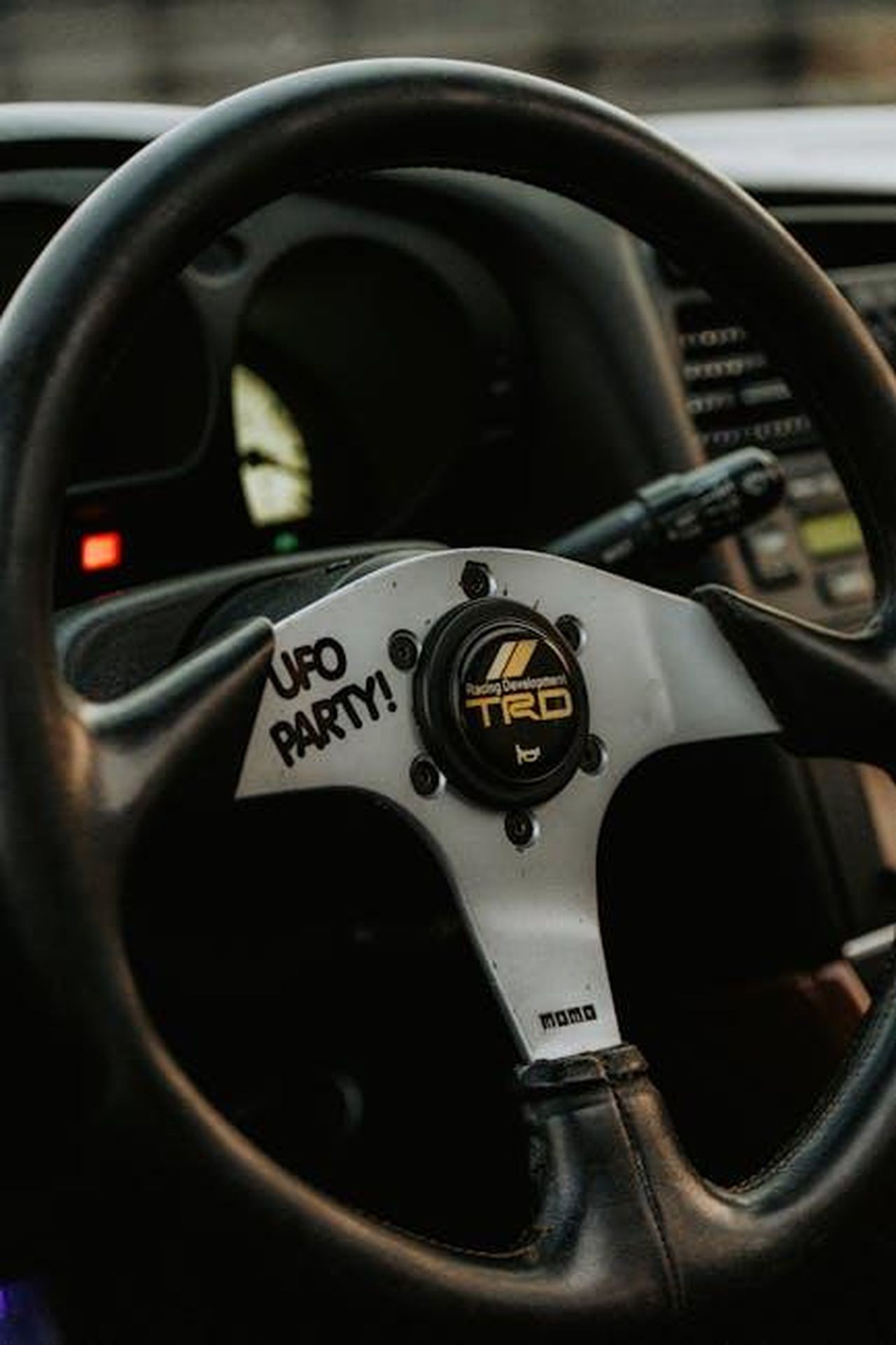 Capacit_di_produzione_di_TRD_unanalisi_approfondita_mmGXfzAeOD - Veicoli24 Source: Luke Miller - pexels - Detailed view of a vintage car's steering wheel featuring the TRD logo and 'UFO Party!' text, highlighting classic automotive design.