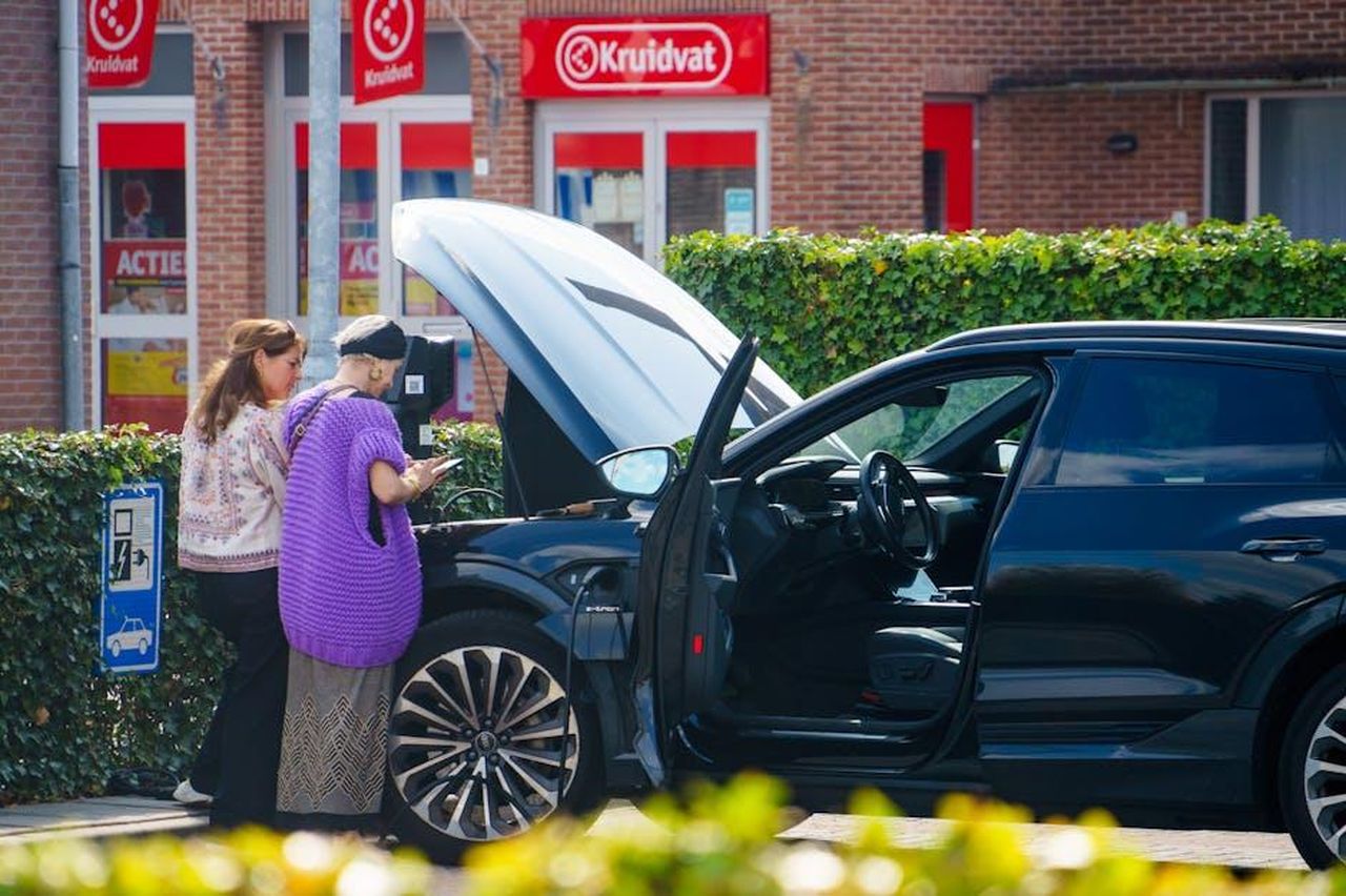 Caratteristiche_di_ricarica_del_Honda_Prologue_2025_ZsgkskQJEJ - Veicoli24 Source: Freek Wolsink - pexels - Two women stand beside a car with an open hood in front of a store, possibly checking for issues.