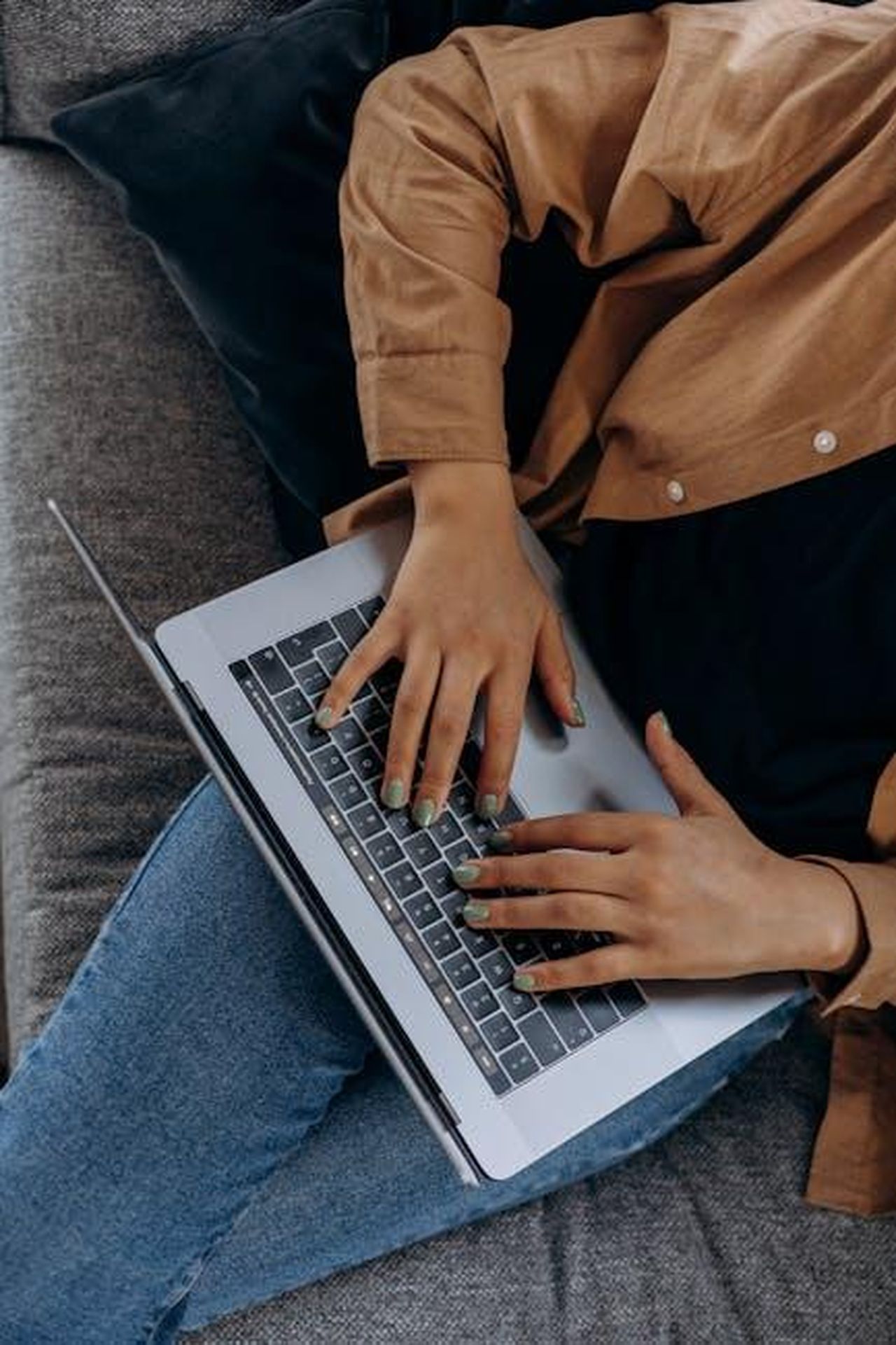 Commenti_dei_CEO_di_Lancia_e_Michelin_mRuR2BNr4V - Veicoli24 Source: Mikhail Nilov - pexels - A person typing on a laptop while seated on a couch with casual attire, perfect for remote work imagery.
