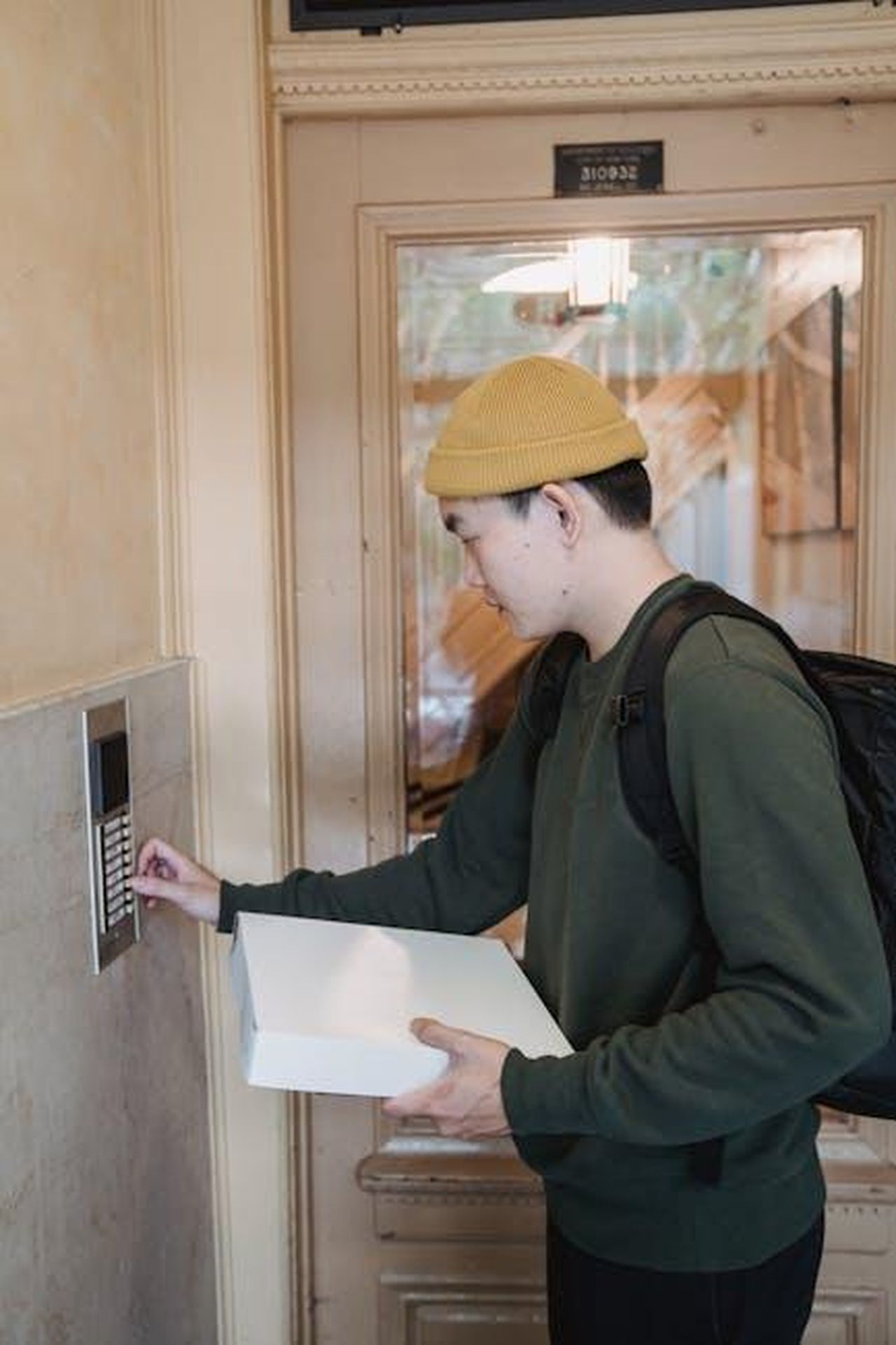 Contatti_Stampa_RxtpTRRIh8 - Veicoli24 Source: Mike Jones - pexels - Asian male courier in beanie delivers package, pressing doorbell indoors.