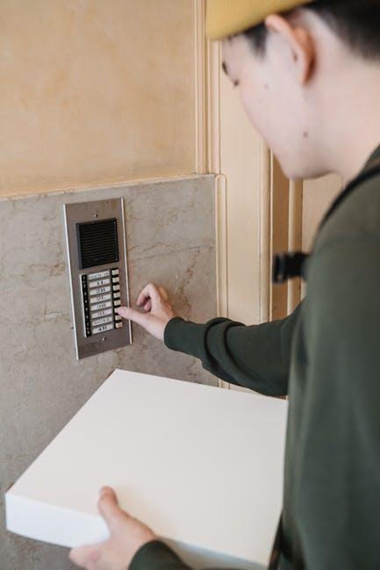 Contatti_Stampa_xOx5HPnBTJ - Veicoli24 Source: Mike Jones - pexels - A delivery person presses the intercom button while holding a package at an entrance.