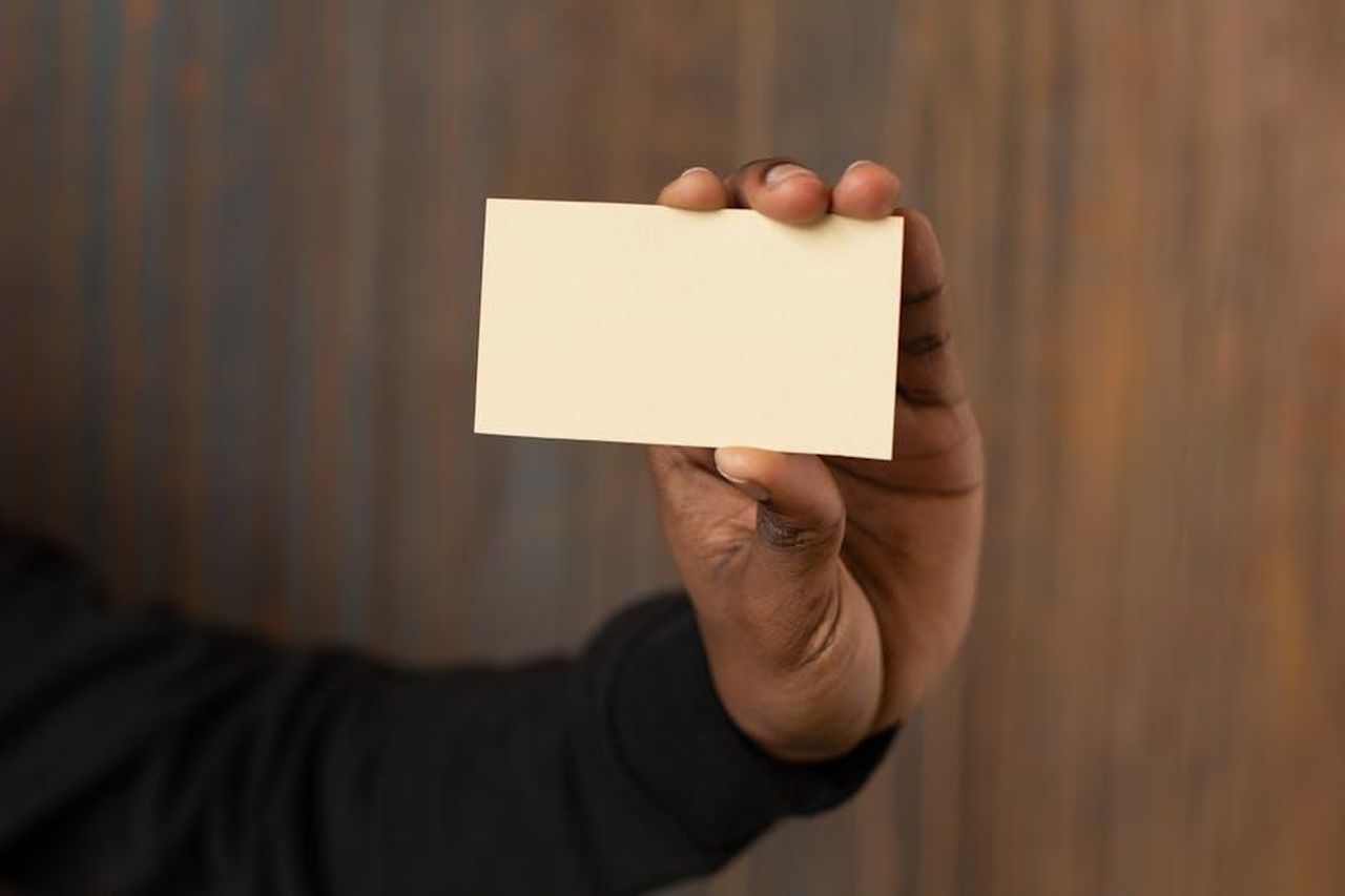 Contatto_SNG_BBqK91UXV4 - Veicoli24 Source: Monstera Production - pexels - A close-up shot of an unrecognizable man holding a blank business card against a wooden background.