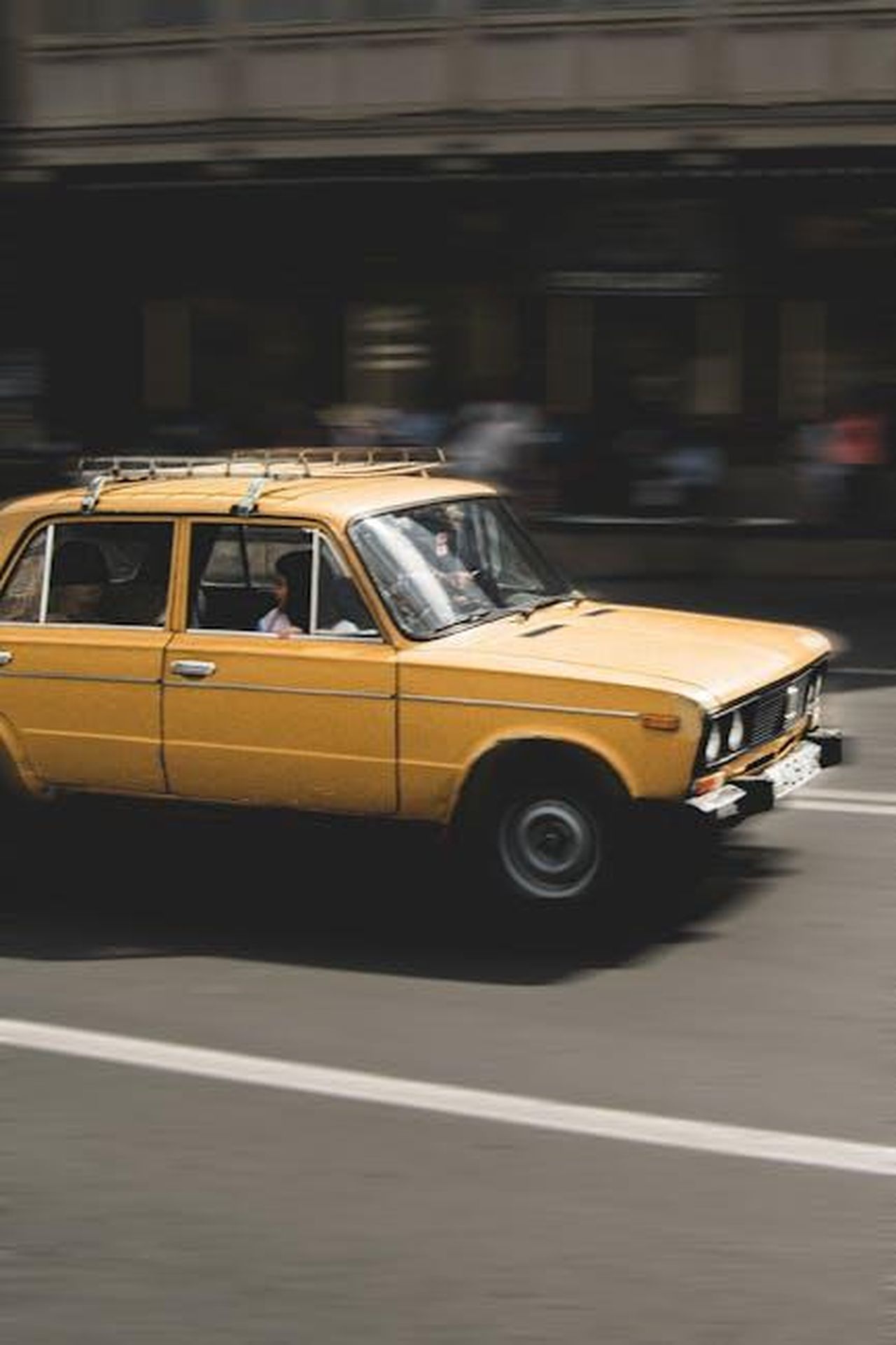 Costruzione_del_Lada_Gigante_con_Due_Motori_LLtHWOjk9v - Veicoli24 Source: Artūras Kokorevas - pexels - A classic yellow car in motion on an urban road in Tbilisi, showcasing speed and vintage charm.