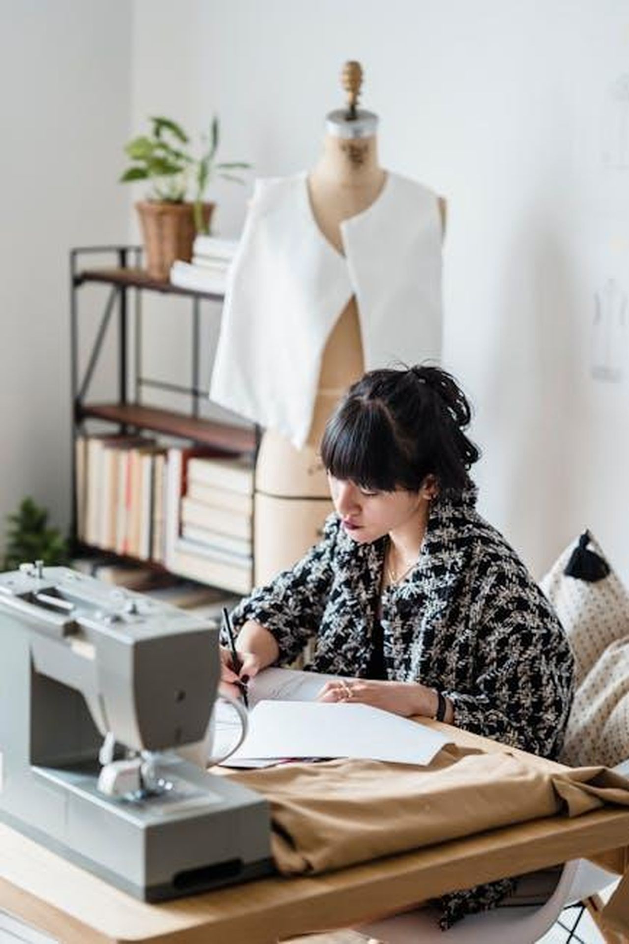Creazione_di_posti_di_lavoro_e_impatto_economico_56fjIsiqJi - Veicoli24 Source: Michael Burrows - pexels - Side view of concentrated female tailor in stylish clothes sitting at table with sewing machine and making sketches in light modern atelier