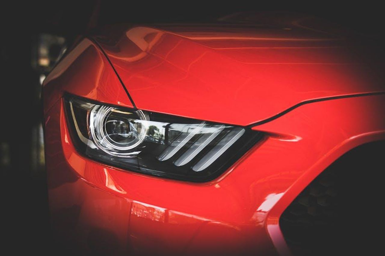 Dettagli_sul_Project_9559_Mh3coCjDt1 - Veicoli24 Source: Vraj Shah - pexels - Detailed view of a red Ford Mustang's headlight showcasing sleek automotive design.