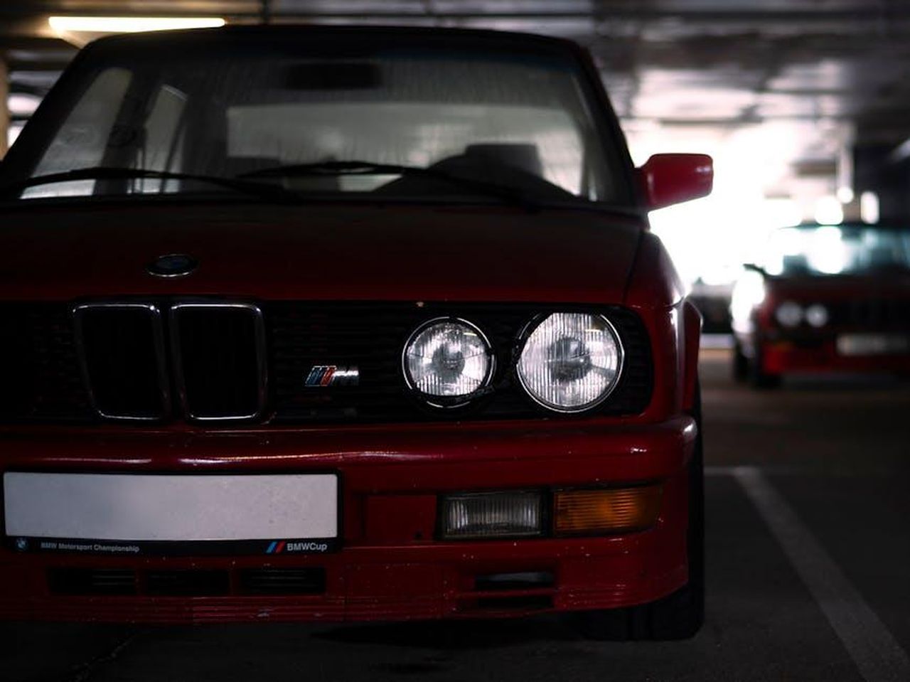 Dichiarazioni_dei_leader_di_BMW_M_Motorsport_efiMJUuVqr - Veicoli24 Source: Vitali Adutskevich - pexels - Front view of a vintage red BMW M series car in a dimly lit parking garage.