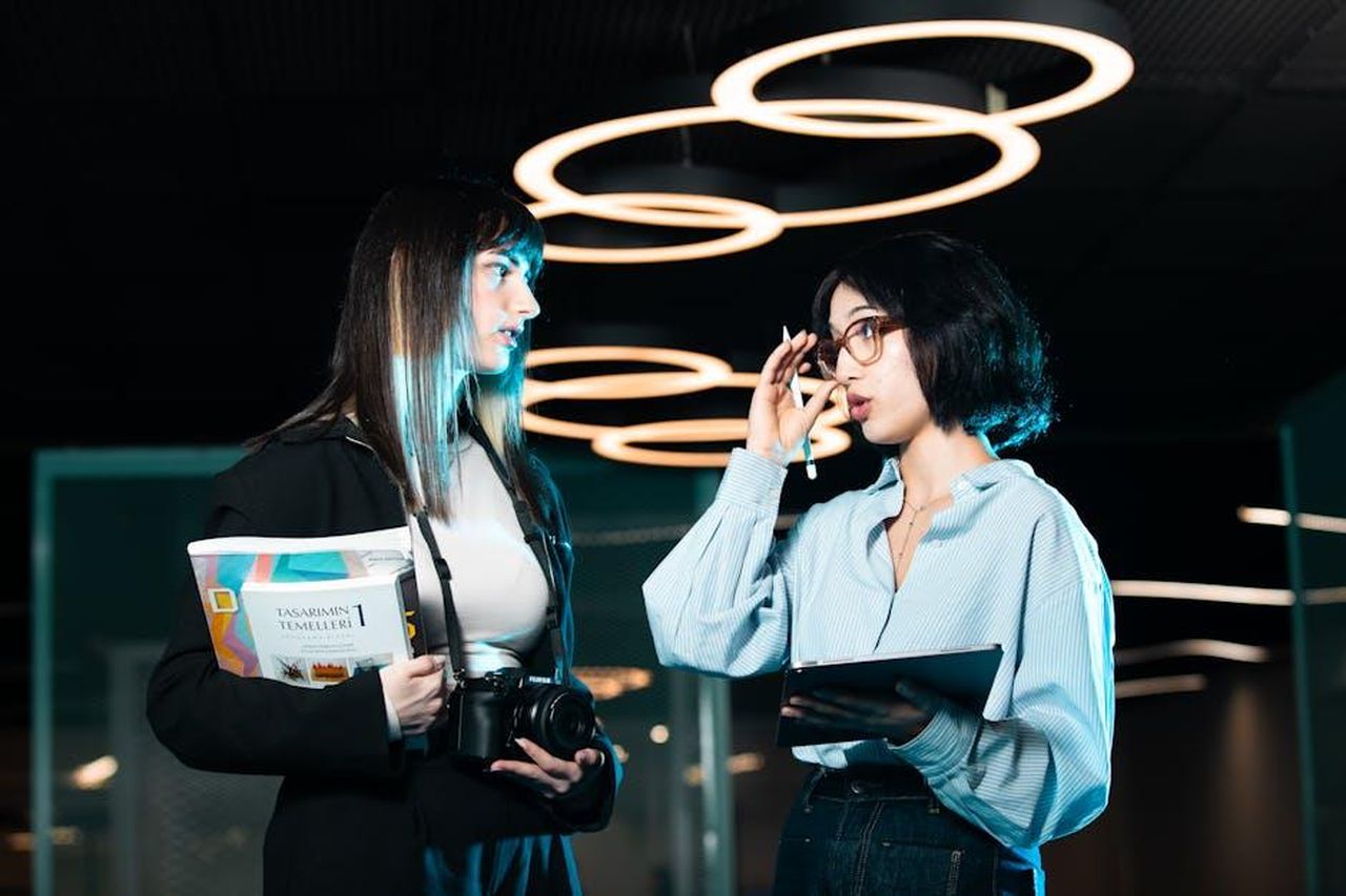 Esperienza_di_Aragon_nel_settore_tecnologico_Y3HxKXjxEU - Veicoli24 Source: Yusuf Timur Çelik - pexels - Two women in a modern office discussing with digital devices, highlighting contemporary teamwork.