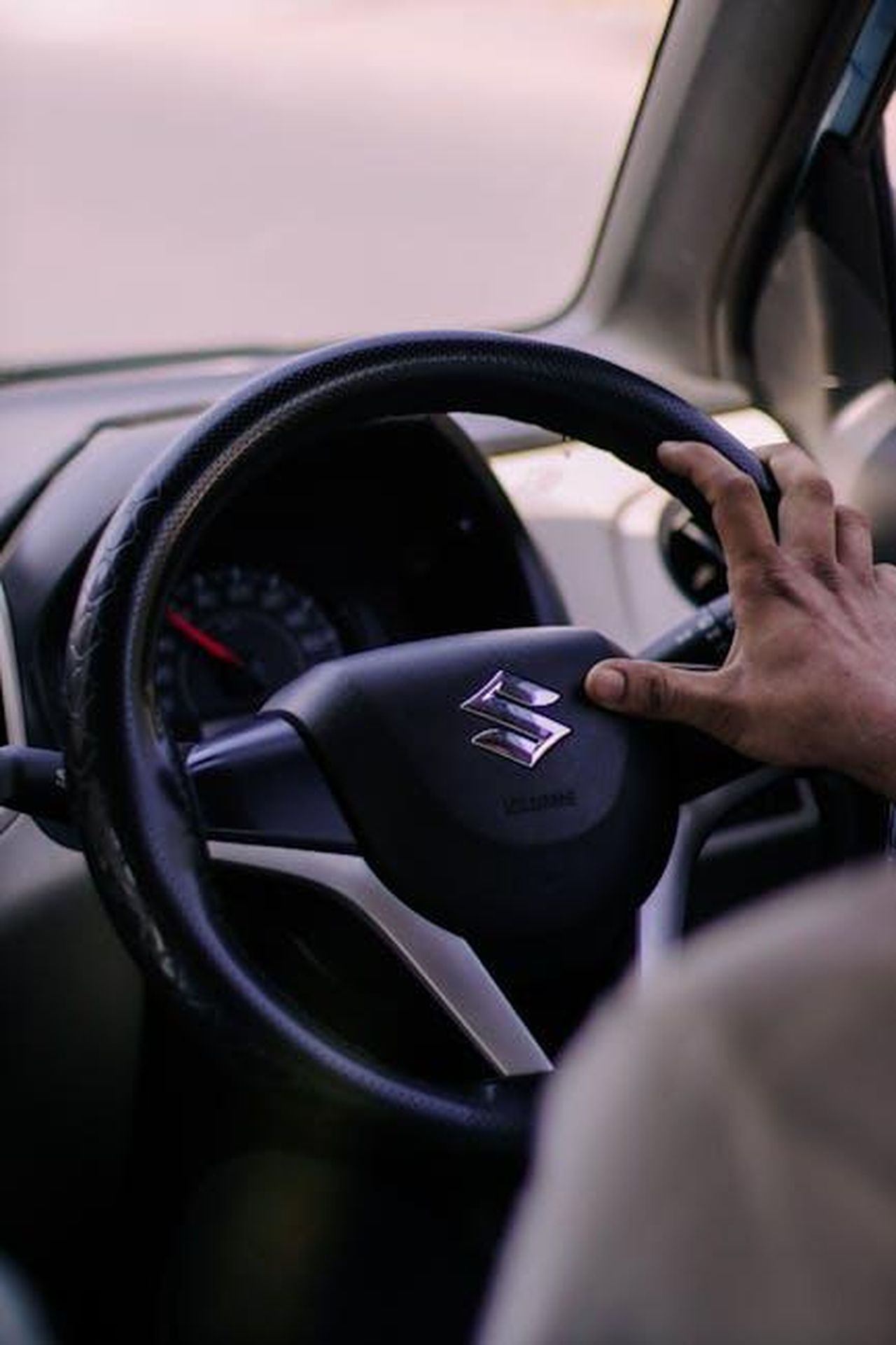 Importanza_della_sicurezza_per_i_consumatori_NvrLDdLy32 - Veicoli24 Source: Jomon Kollannoor - pexels - Close-up of a hand gripping a Suzuki steering wheel in a car interior, showcasing driving focus.
