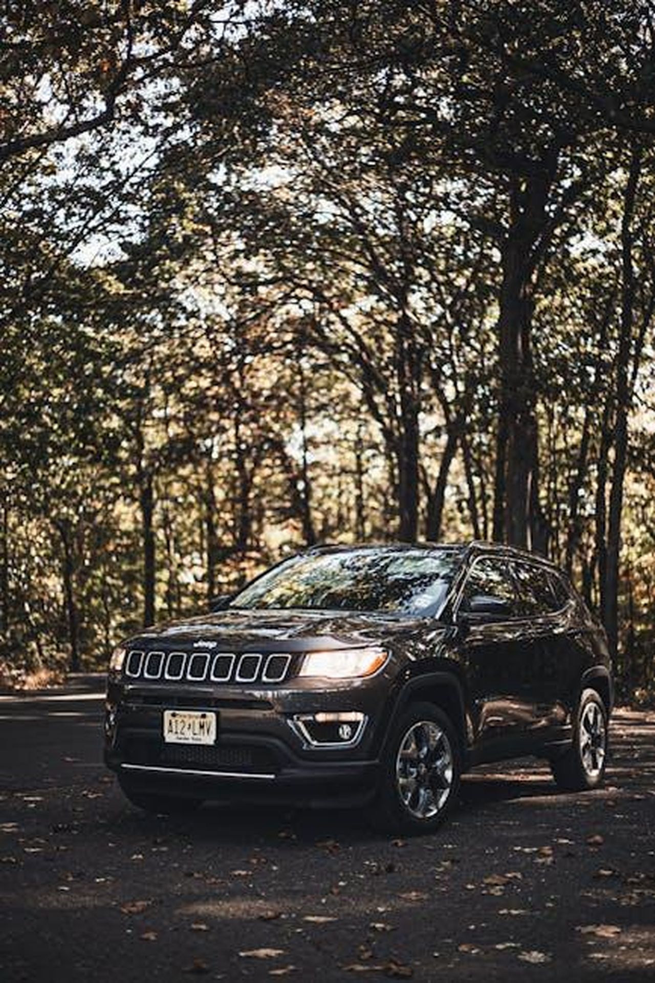 Jeep_Compass_presentazione_globale_e_produzione_europea_simgMvD0M2 - Veicoli24 Source: Keenan Constance - pexels - Black Jeep Compass SUV parked in a wooded area, showcasing nature and a classic vehicle contrast.