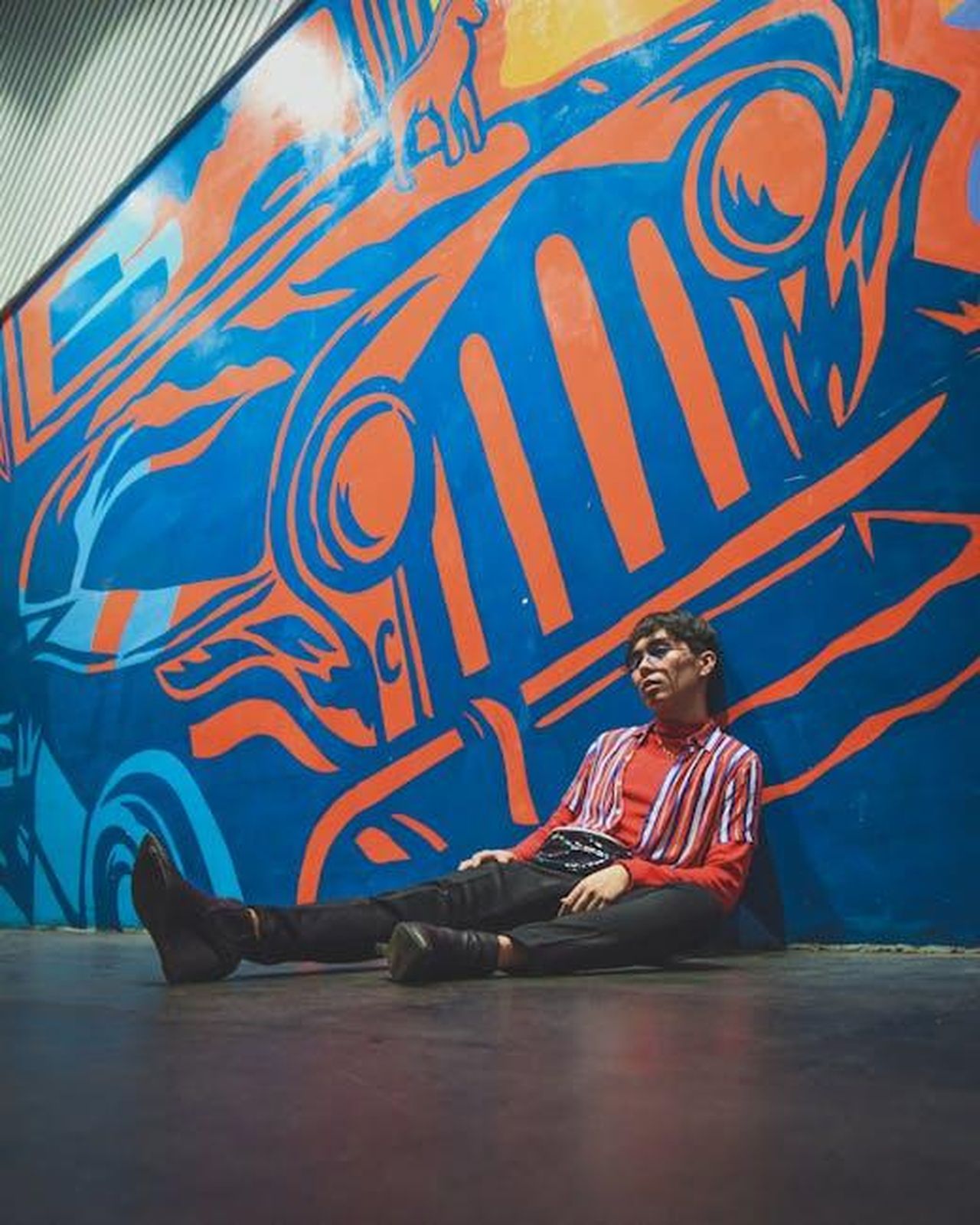 La_creazione_di_Jeep_Avenger_4xe_un_viaggio_dietro_le_quinte_li0KmCkYSp - Veicoli24 Source: Chris Creatives - pexels - A fashionable young man in a striped outfit sits against a bold and colorful street art mural.