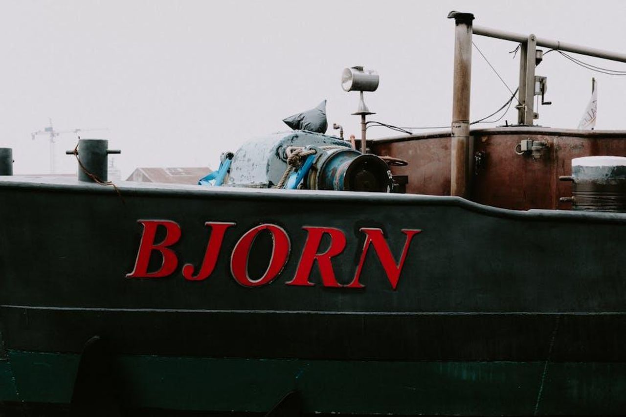 Le_dichiarazioni_di_Bjrn_Lellmann_lolULhVgFh - Veicoli24 Source: Mathias Reding - pexels - Close-up of a rustic boat with 'BJORN' text, conveying an industrial vibe against a cloudy backdrop.