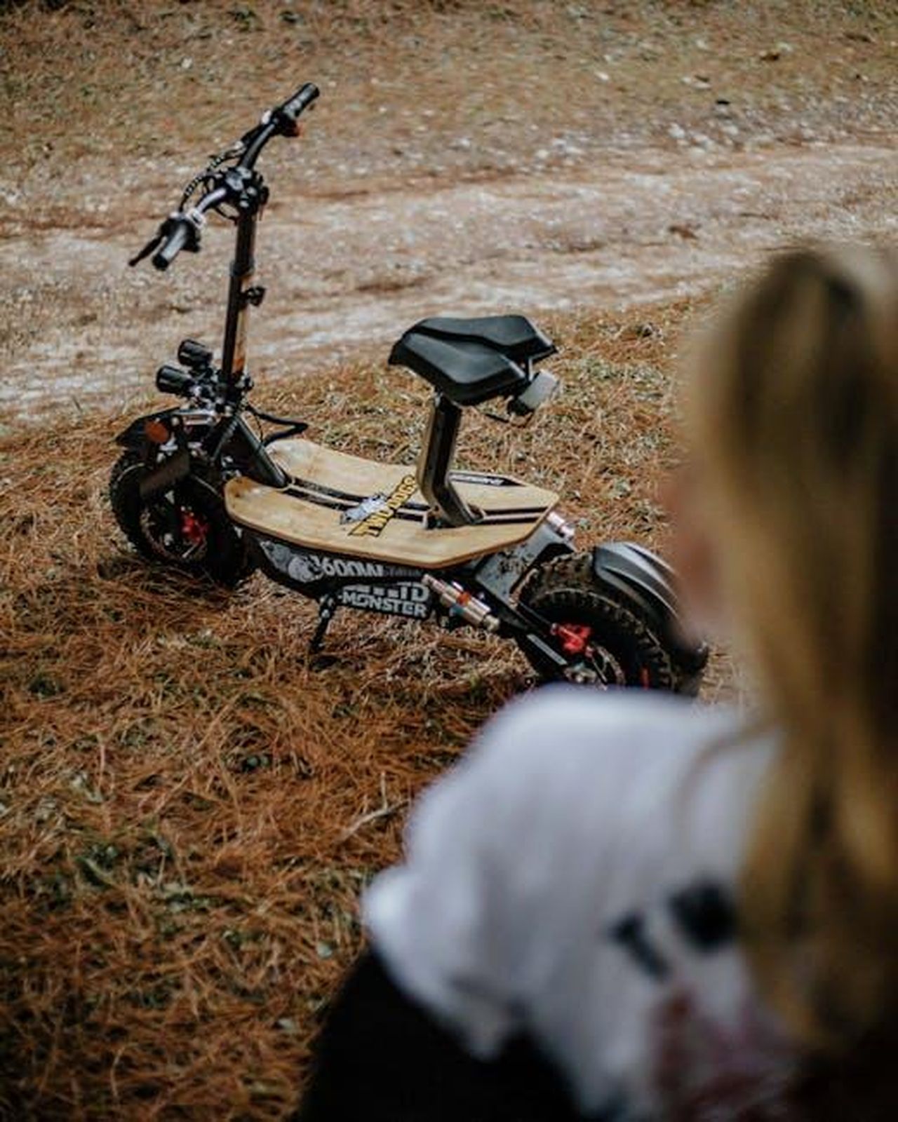 Lentusiasmo_per_i_veicoli_elettrici_va_oltre_la_mobilit_CVClYAs7xF - Veicoli24 Source: Paulo Freitas - pexels - Parked electric scooter on a dirt path with person blurred in foreground.