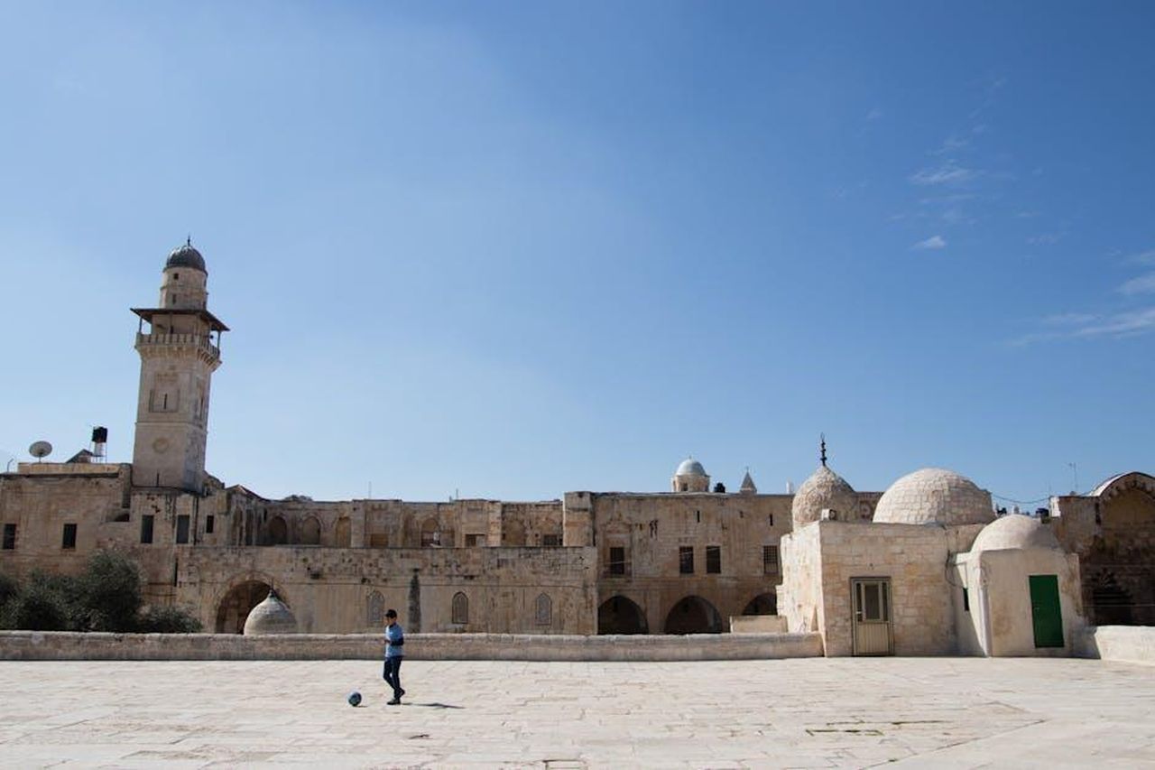 Leredit_di_MINI_e_il_futuro_del_calcio_inglese_v2wU7V1FIN - Veicoli24 Source: BECCA SIEGEL - pexels - A young boy kicking a ball in front of an ancient mosque with domes and towers under a clear blue sky.