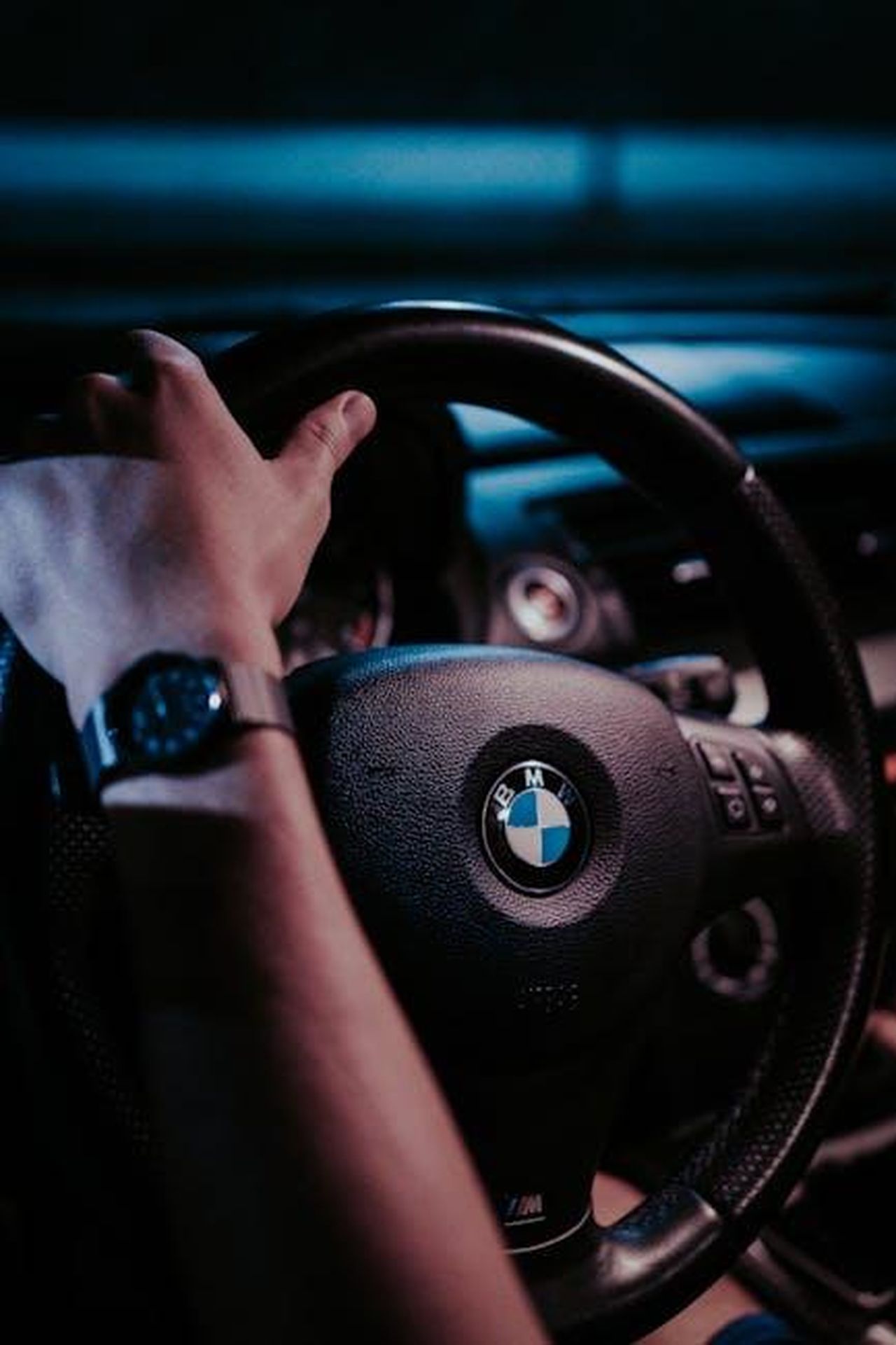 Performance_dei_Brand_ARvLjhTNm8 - Veicoli24 Source: Luis Quintero - pexels - Close-up of a hand on a BMW steering wheel at night, showcasing the car interior.