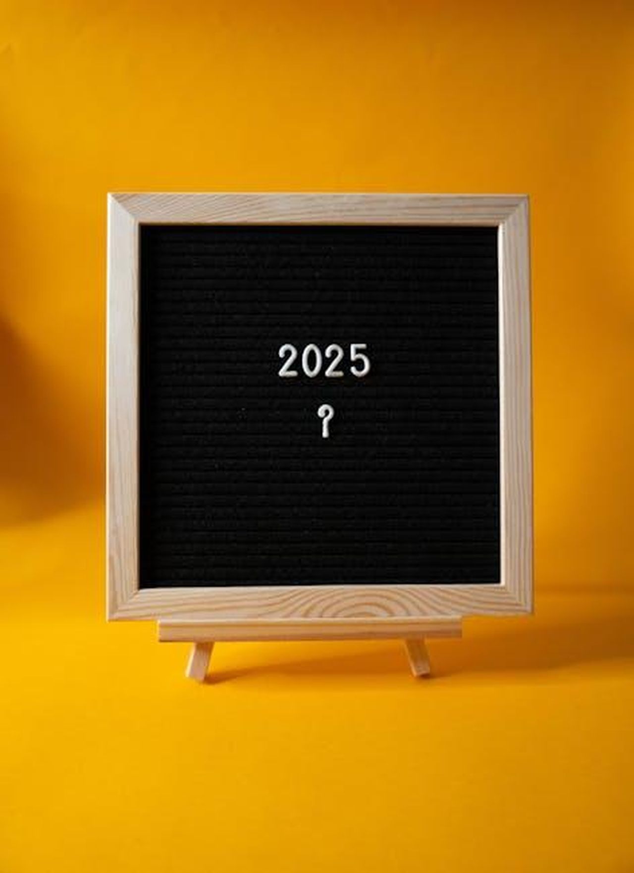Prospettive_per_il_2025_X4l8cG11uW - Veicoli24 Source: Viridiana Rivera - pexels - A wooden framed blackboard with '2025' on a bright yellow background.
