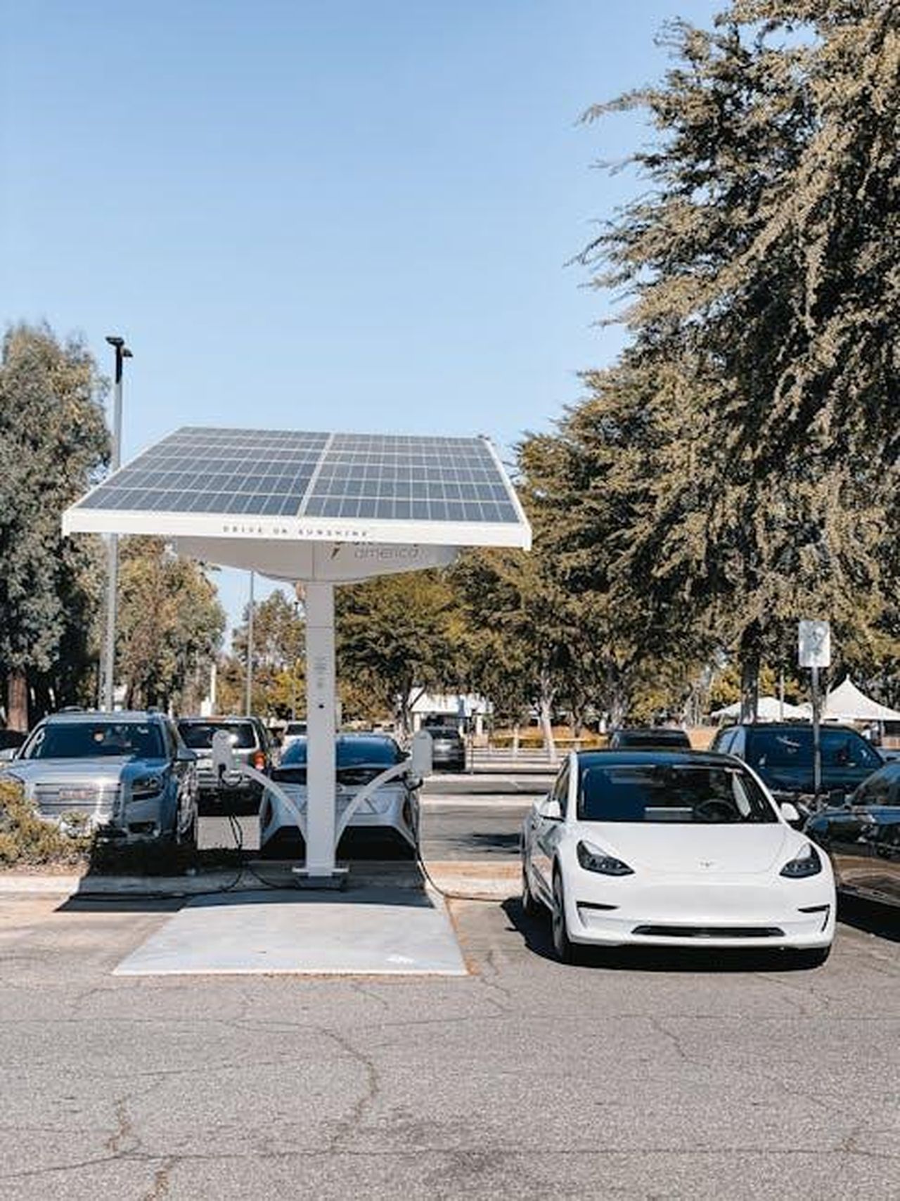 Punti_di_forza_della_nuova_Junior_Ibrida_Q4_7RSd6EFcjd - Veicoli24 Source: Kindel Media - pexels - A white electric car charging under a solar panel in an urban setting, showcasing renewable energy use.