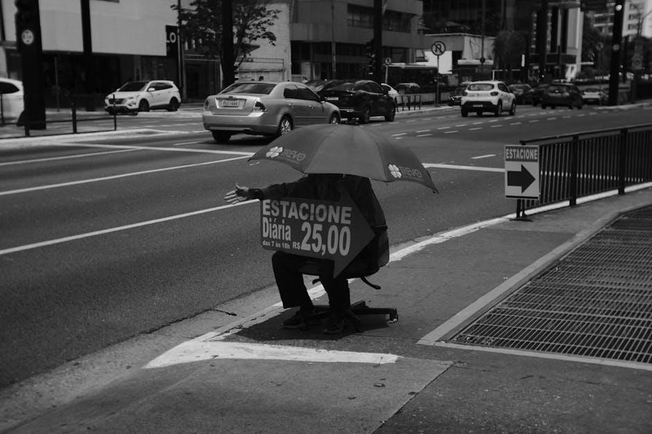 Quanto_costa_la_Lucid_Air_2025_bI7f7u06ra - Veicoli24 Source: Leo Sacchi - pexels - Black and white photo of a person holding a parking sign under an umbrella on a busy city street.