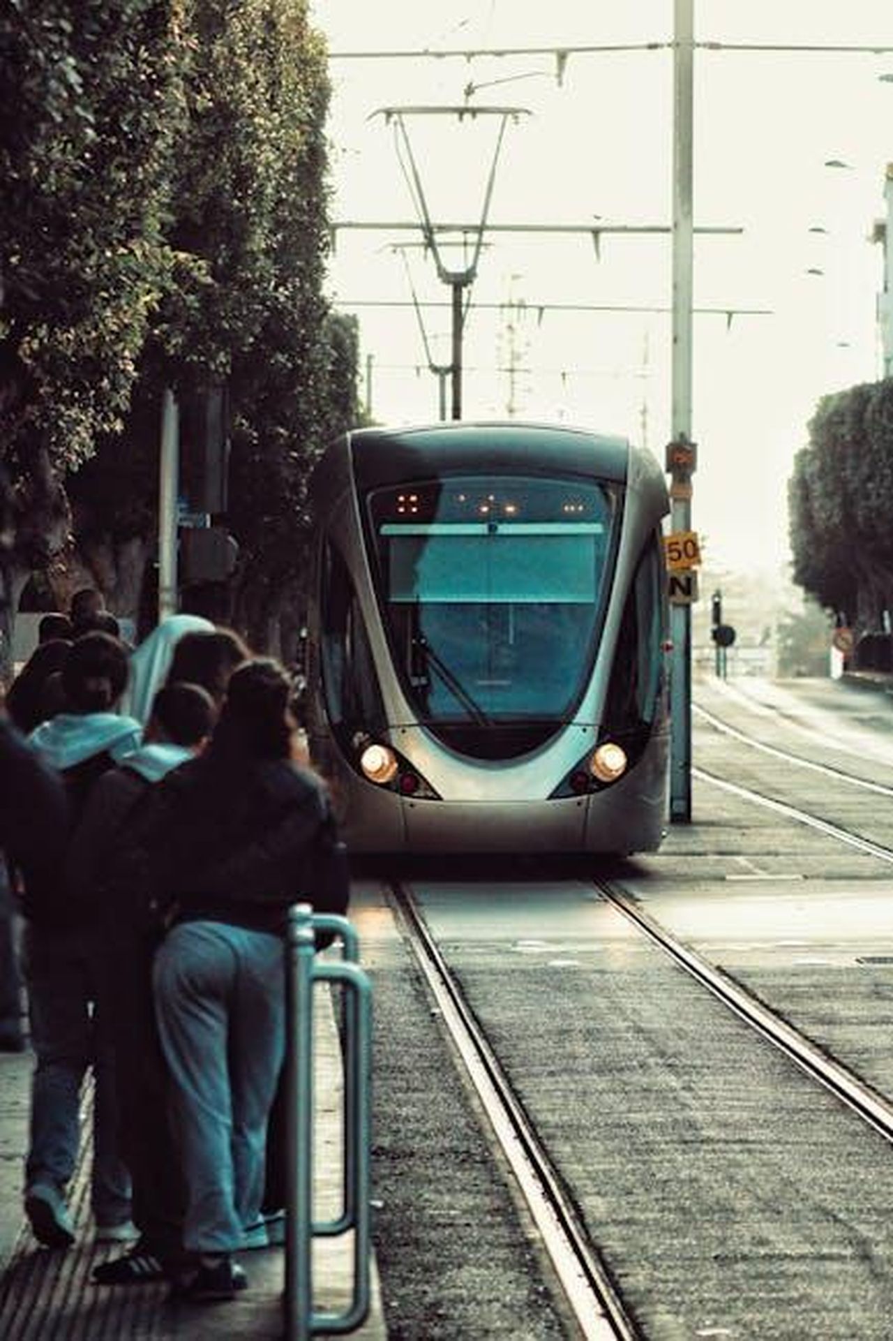 Risultati_principali_dellindagine_DRQkynjZIm - Veicoli24 Source: yassir draka - pexels - A sleek tram approaches an urban street station with people waiting on the side.