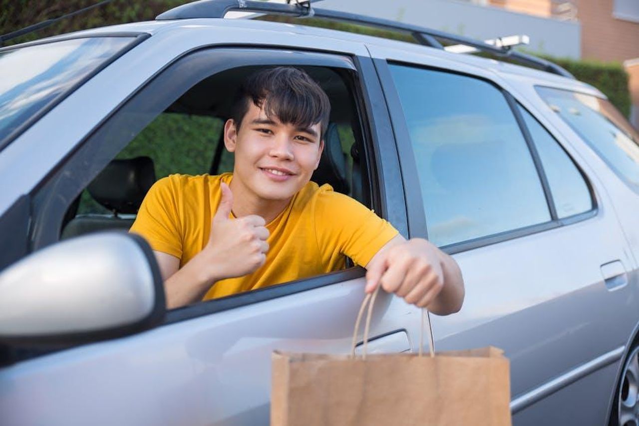Servizio_di_courtesy_car_durante_la_Design_Week_eqqGubFcLL - Veicoli24 Source: Kampus Production - pexels - Smiling courier in car delivering a paper bag, offering friendly service.
