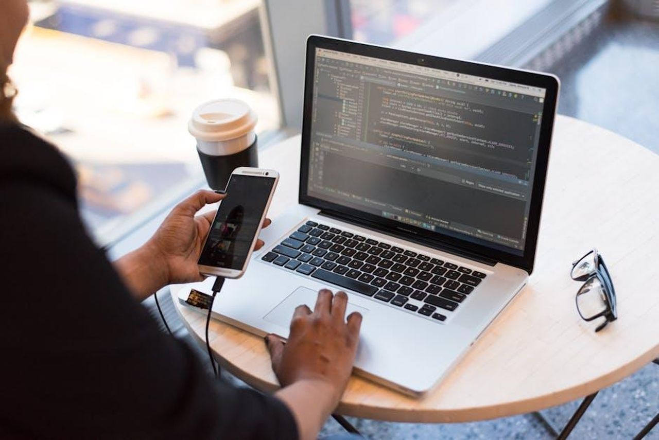 Sviluppo_software_per_la_Neue_Klasse_F4gb5sx6h6 - Veicoli24 Source: Christina Morillo - pexels - Developer working remotely, coding on a laptop with phone in hand, showcasing modern work culture.