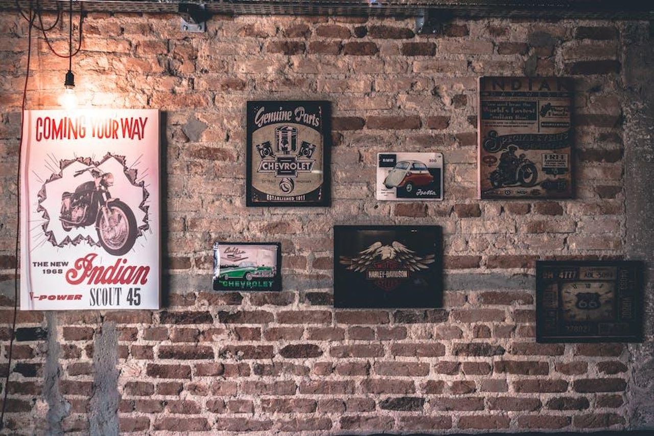 Un_anniversario_in_tutto_il_mondo_Sh4qlX2aV1 - Veicoli24 Source: Kaique Rocha - pexels - Retro wall art featuring motorcycle and car signs on a rustic brick wall.