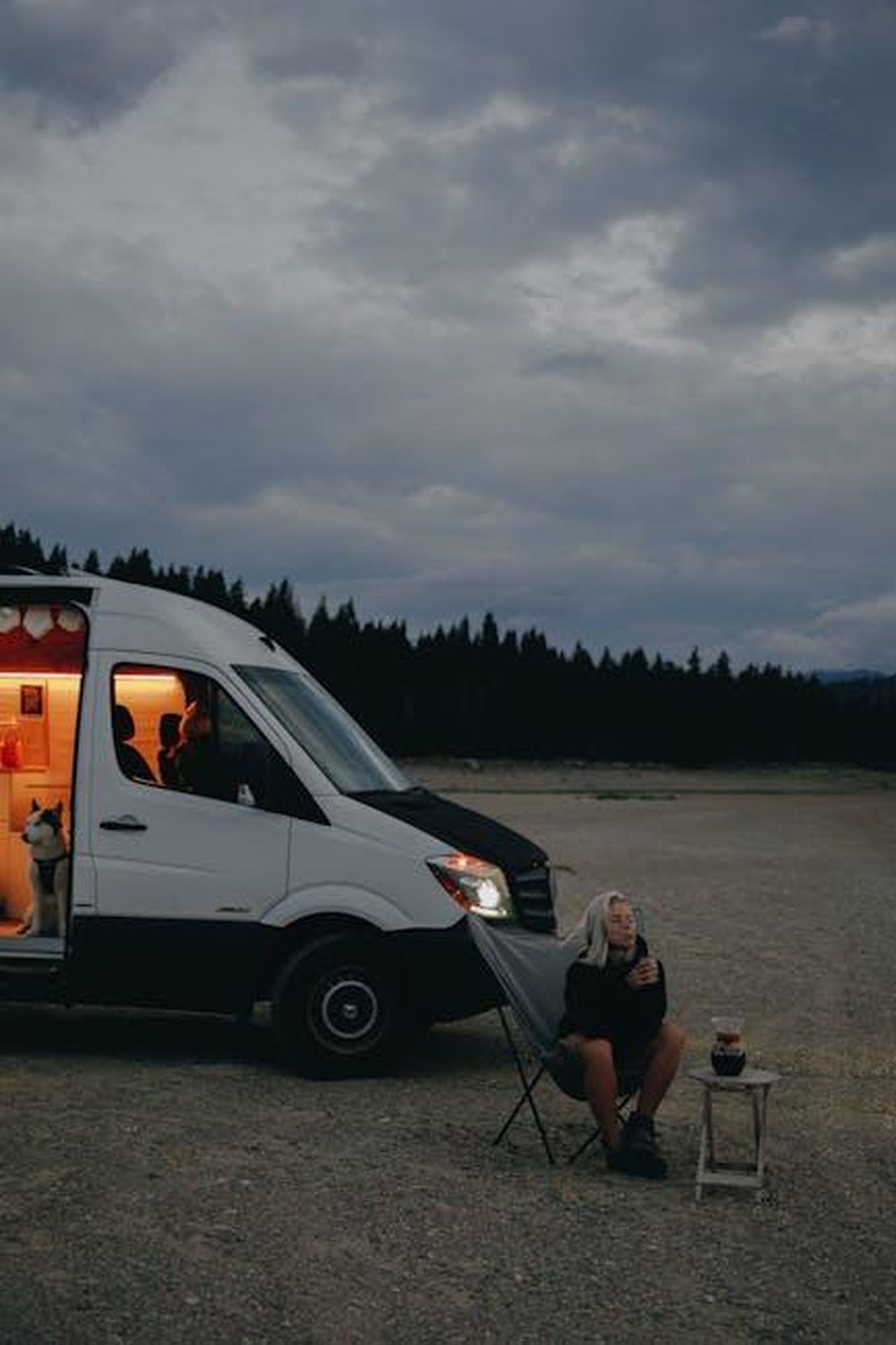 Un_anniversario_per_un_talento_eccezionale_OjWPiUNrgV - Veicoli24 Source: PNW Production - pexels - An adult woman relaxes outside a campervan, sitting under cloudy skies with her dog by her side.